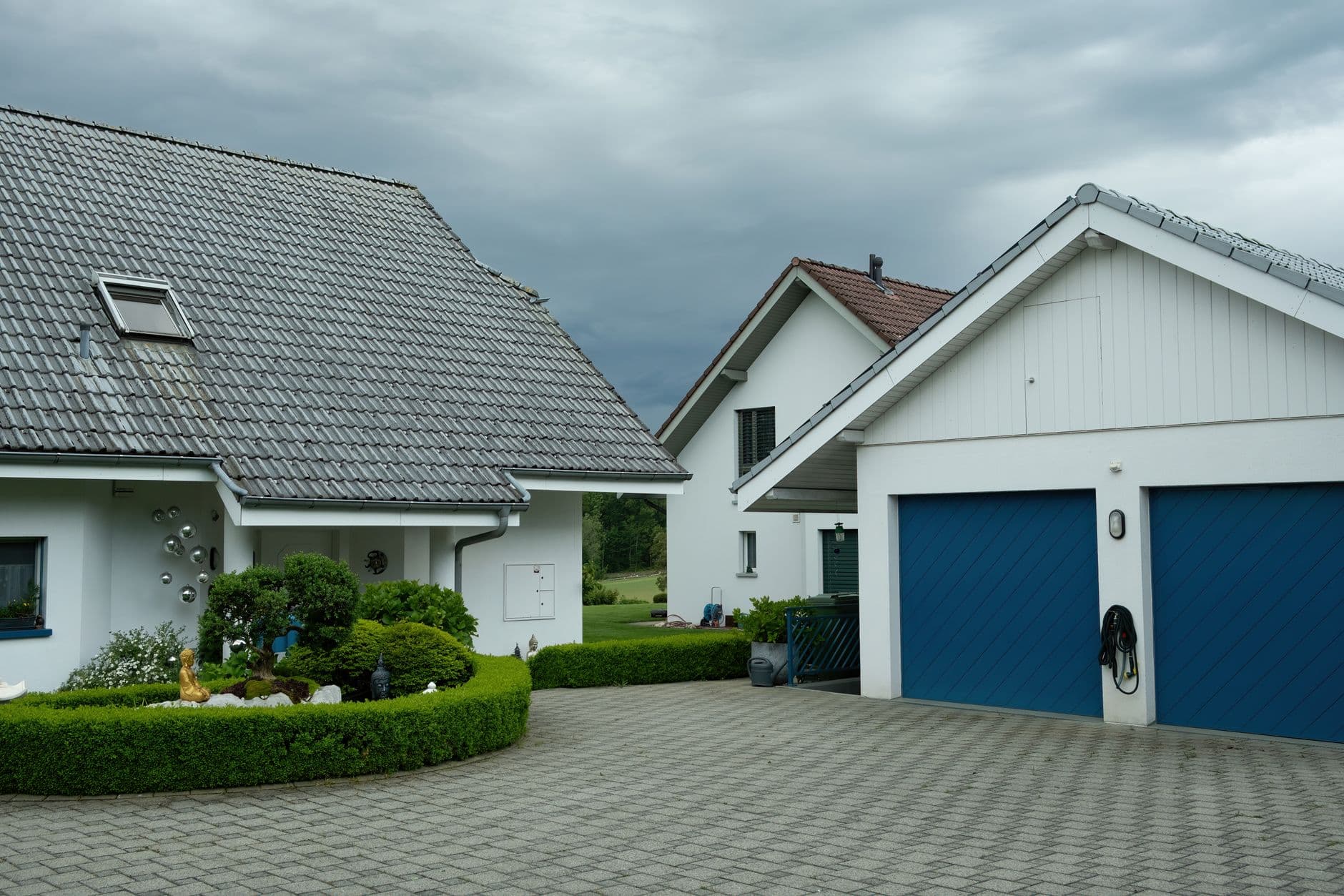 Witte woningen met grijze pannendaken, blauwe garagepoorten en een geplaveide oprit onder donkere wolken