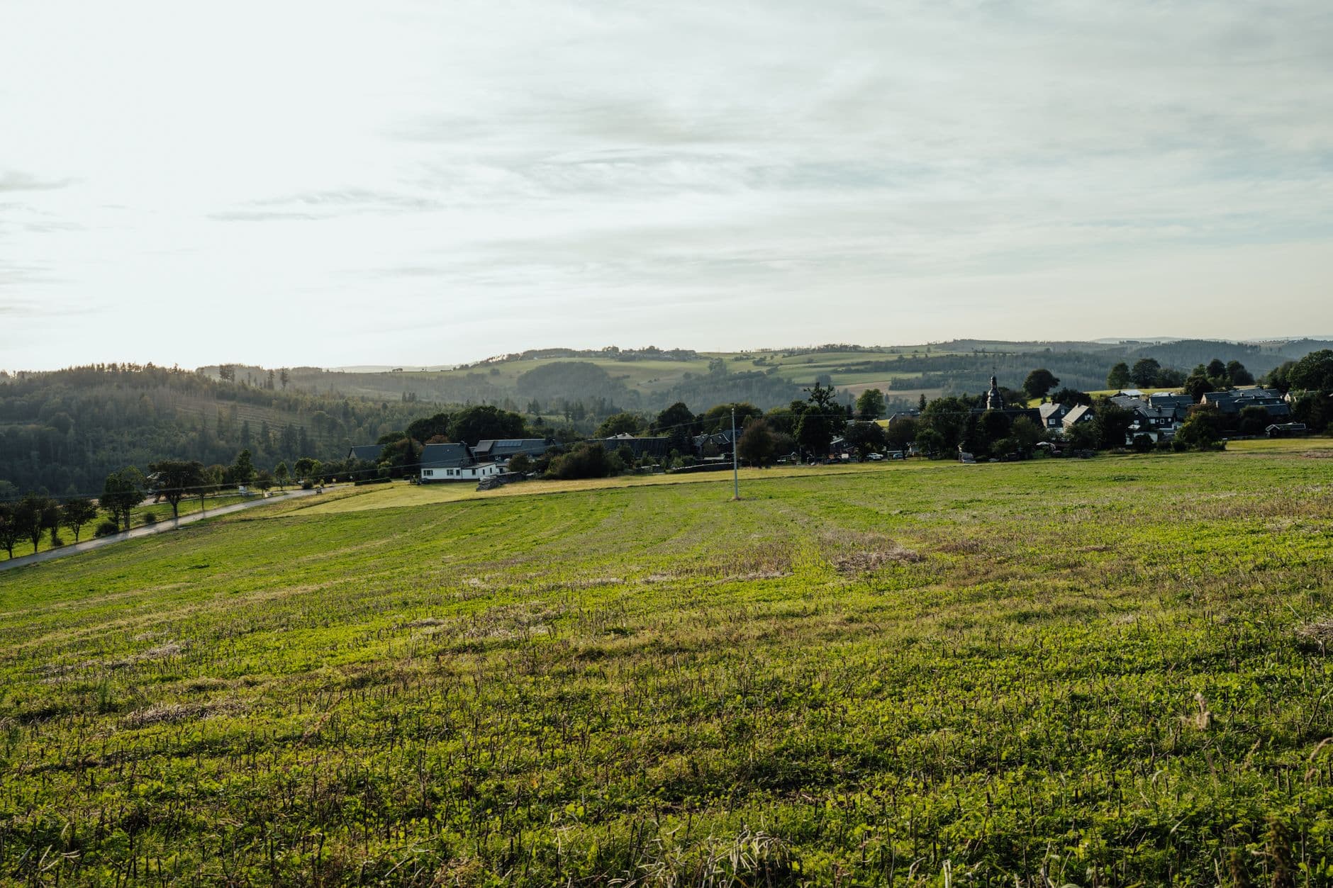 Glooiend groen akkerland met een dorp en beboste heuvels op de achtergrond