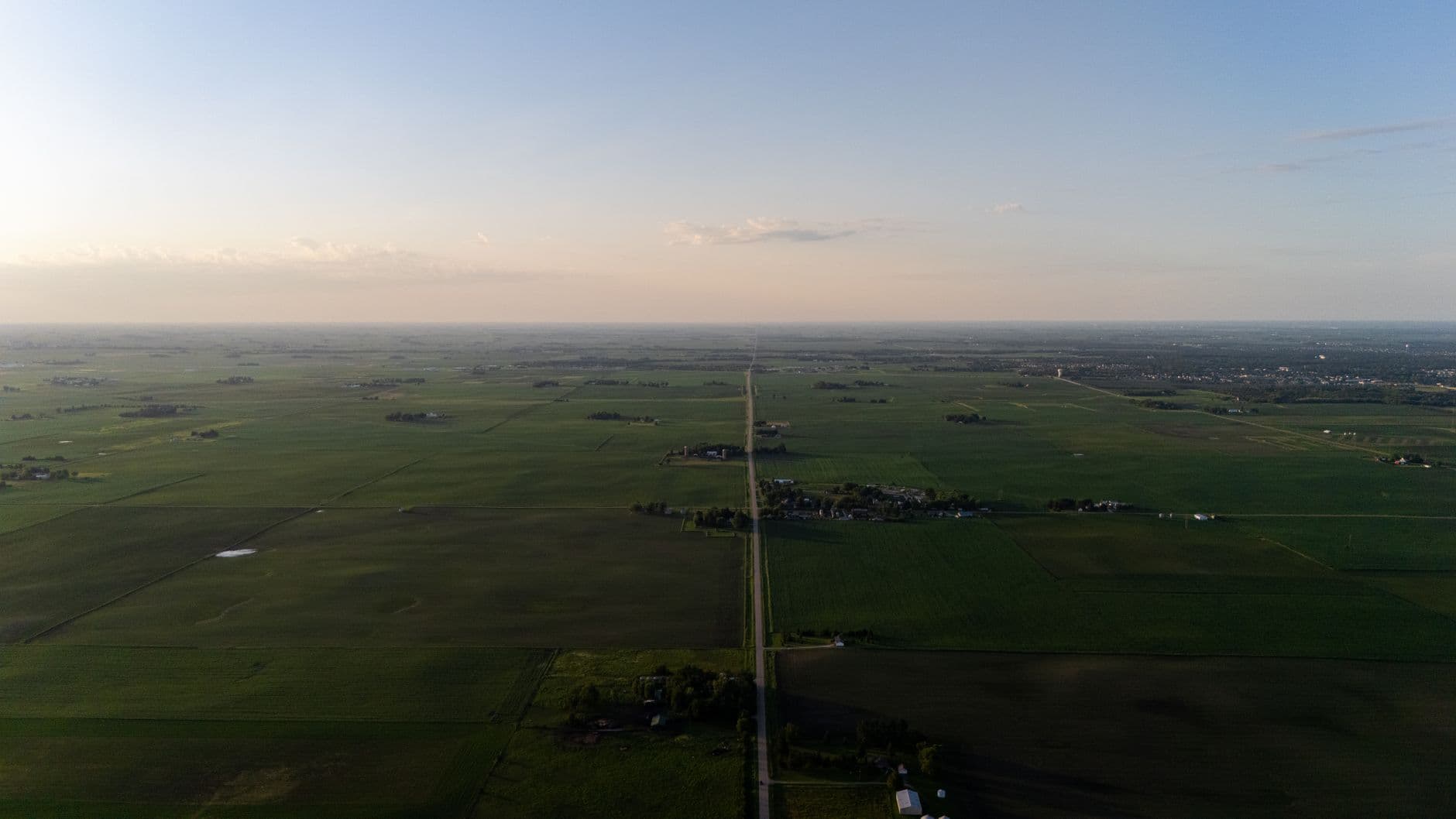 Luchtbeeld van vlak akkerland met een rechte landweg en verspreide boerderijen bij zonsondergang