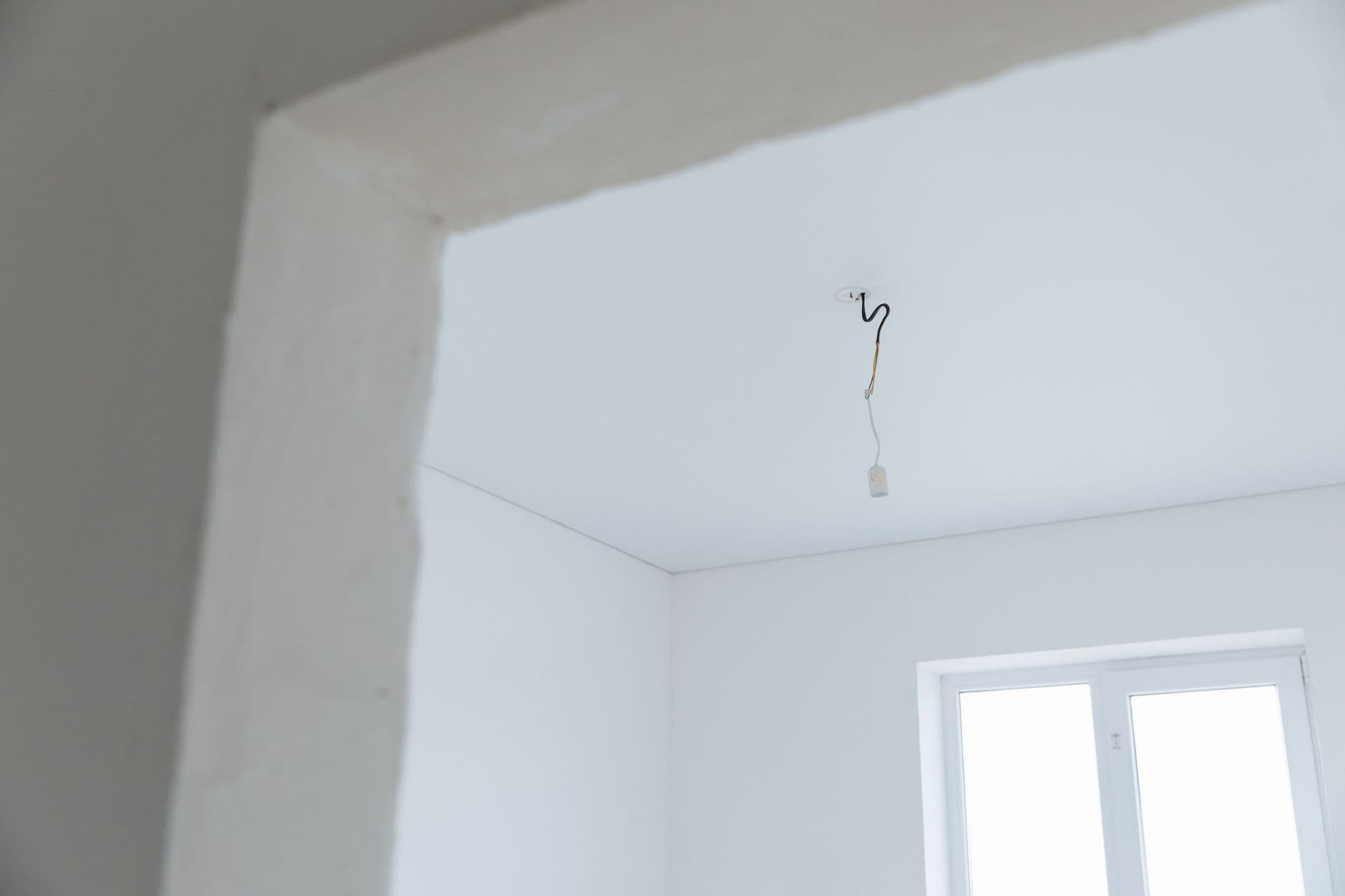 Witte, pas gepleisterde kamer met een losse elektriciteitsdraad aan het plafond en een raam