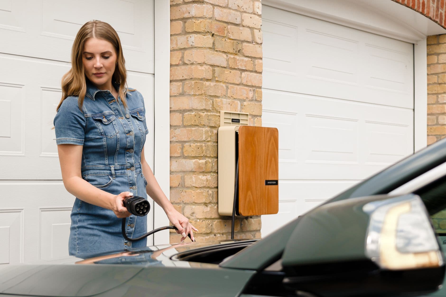 Vrouw sluit een elektrische wagen aan op een laadpaal aan een bakstenen gevel