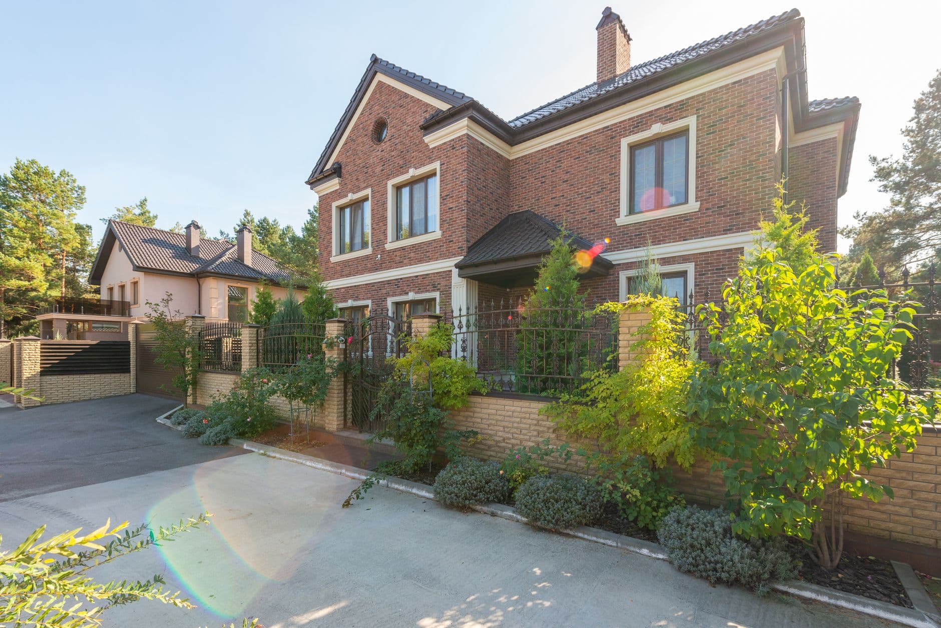 Bakstenen villa met donker pannendak, lage tuinmuur en oprit in de zon