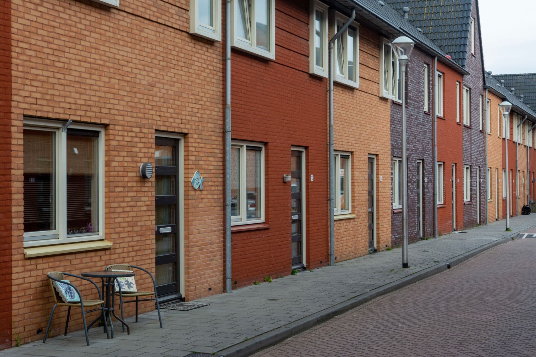 Rij bakstenen rijwoningen in verschillende kleuren langs een rustige straat met stoep