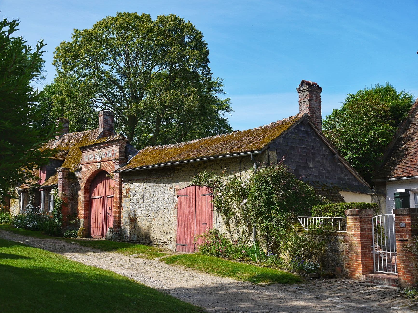 Oude hoeve met bakstenen poort, rode schuurdeuren en een mosbegroeid pannendak in de zon