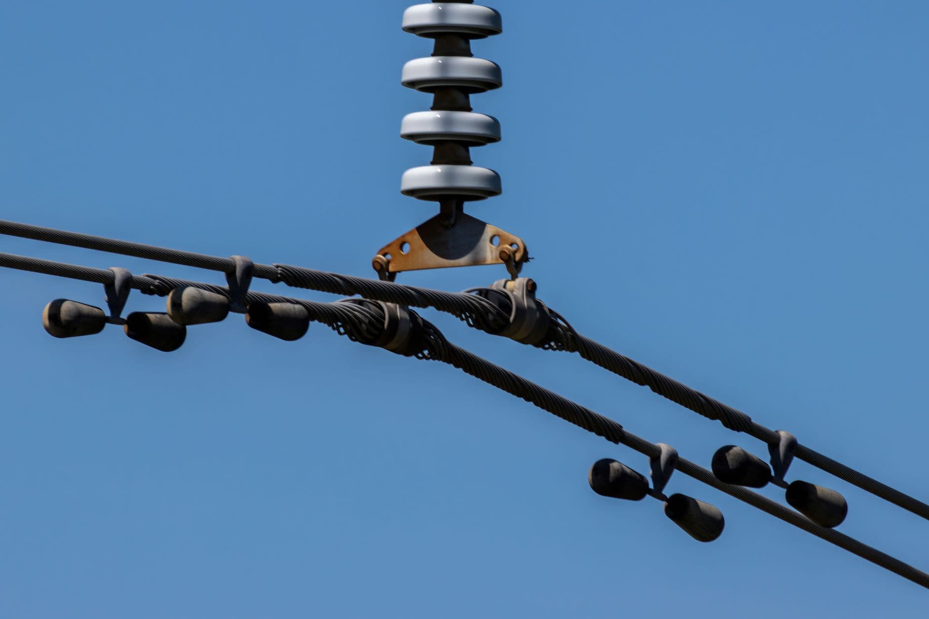Isolator en bovengrondse stroomkabels met trillingsdempers tegen een strakblauwe lucht