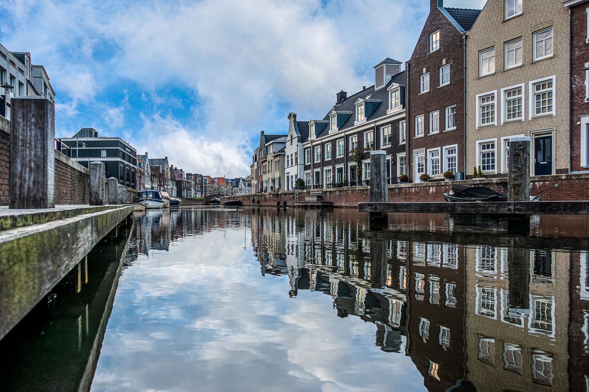 Rij bakstenen woningen langs een rustige gracht die de gevels en de wolkenlucht weerspiegelt