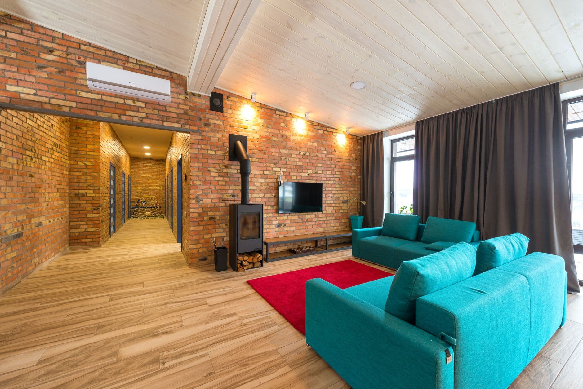 Woonkamer met bakstenen muren, airco-unit, houtkachel, blauwe zetels en een rood tapijt