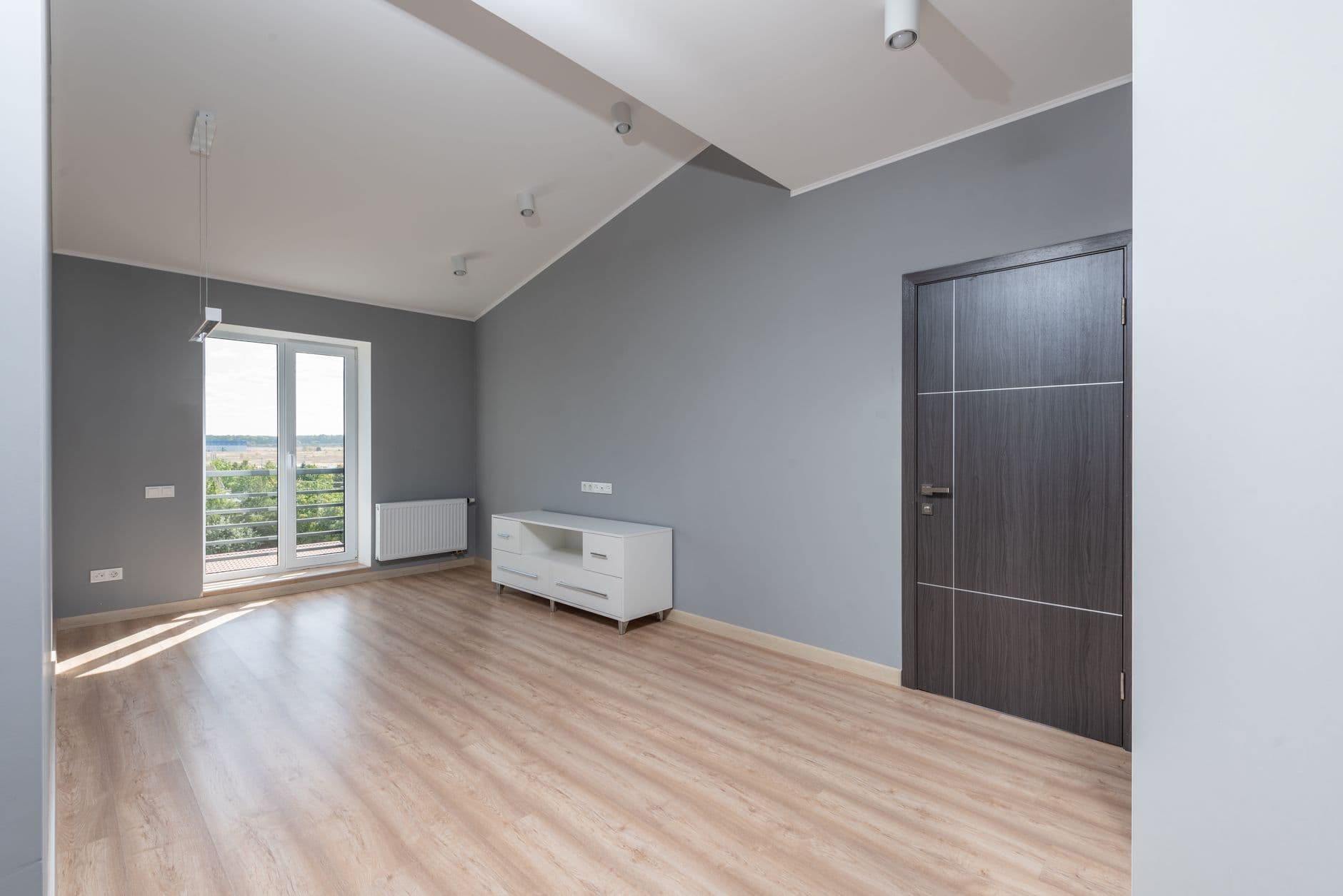 Lege, lichte zolderkamer met houten vloer, inbouwspots, stopcontacten en een radiator