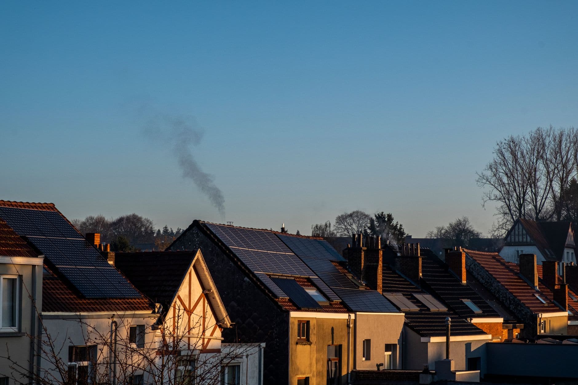 Daken van een rij woningen met zonnepanelen onder een heldere blauwe lucht