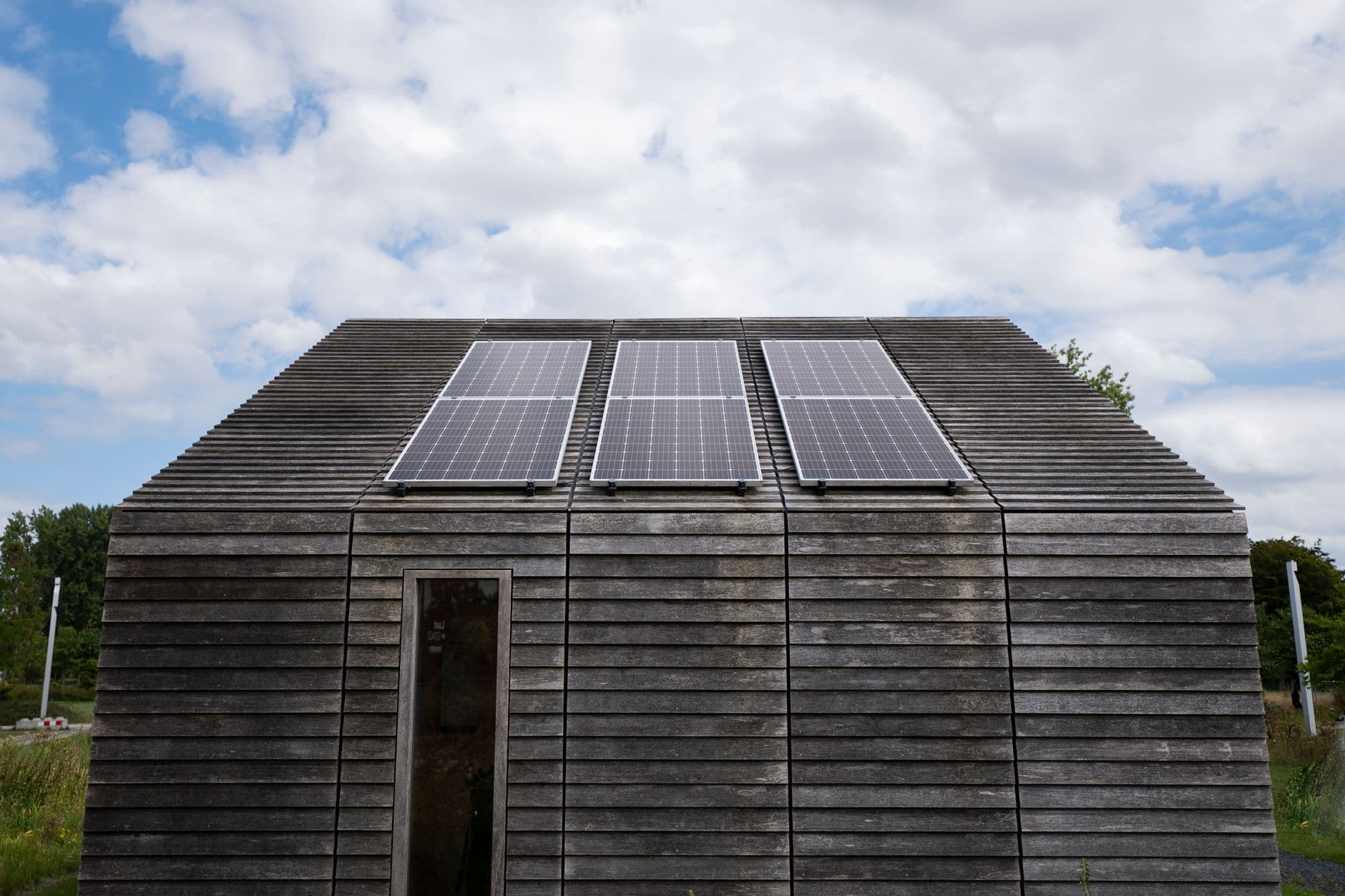 Woning met houten gevelbekleding en drie zonnepanelen op het dak onder een bewolkte lucht