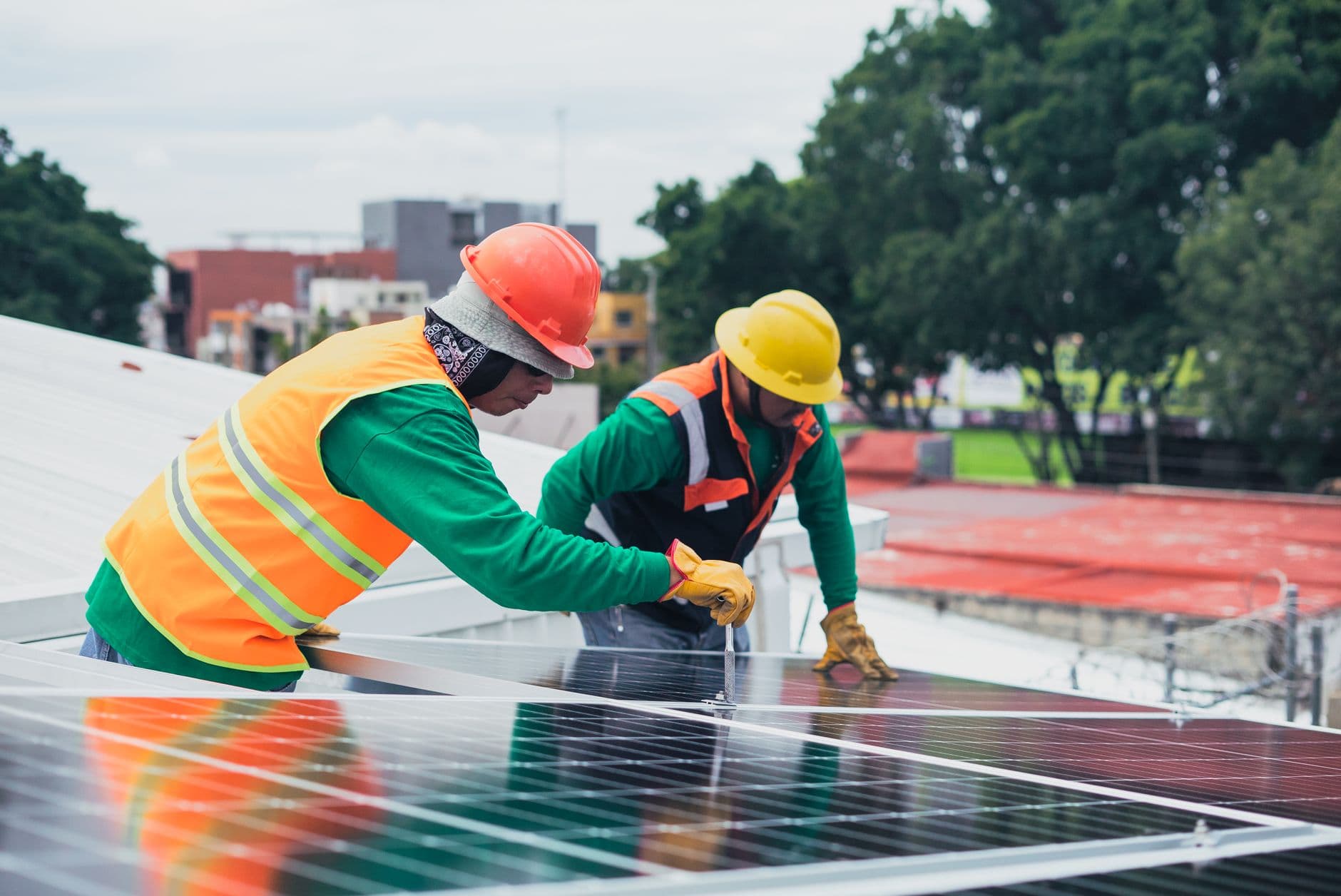 Twee installateurs met helm en veiligheidshesje plaatsen zonnepanelen op een plat dak