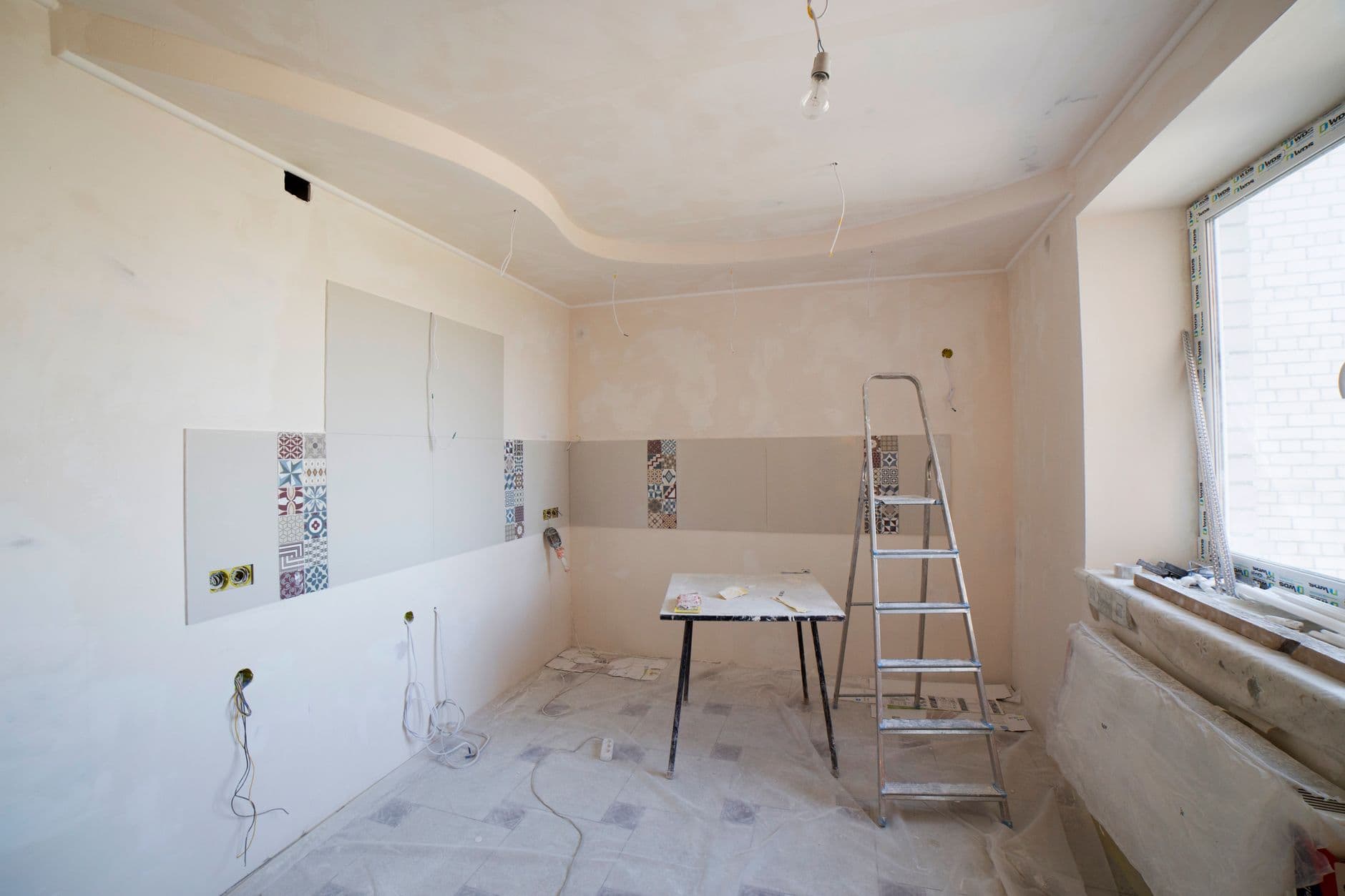 Keuken in renovatie met losse elektriciteitskabels uit de wand, een ladder en een werktafel
