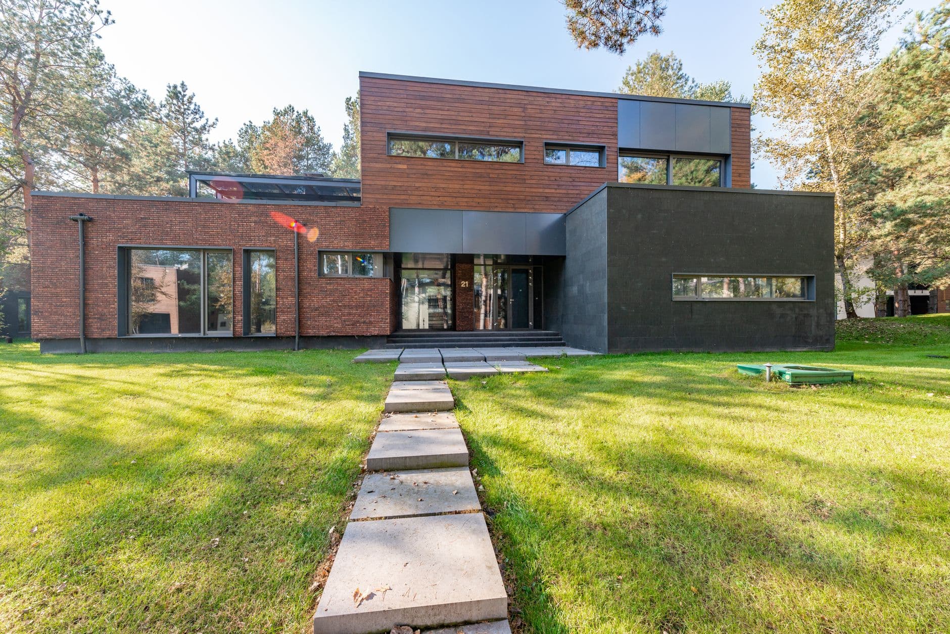 Moderne woning met een gevel in rode baksteen en glas, met een tuinpad over een groen gazon