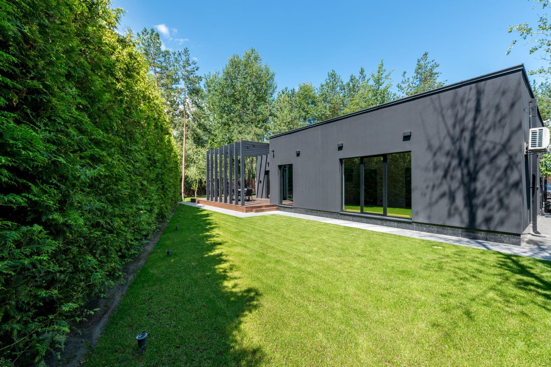 Moderne gelijkvloerse woning met donkere gevel en grote ramen naast een verzorgd gazon en een haag