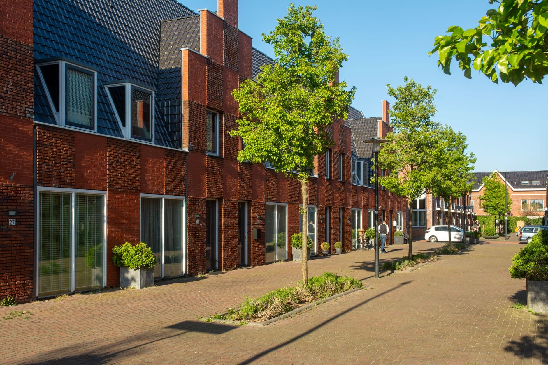 Rij moderne rijwoningen in rode baksteen langs een zonnige straat met jonge bomen