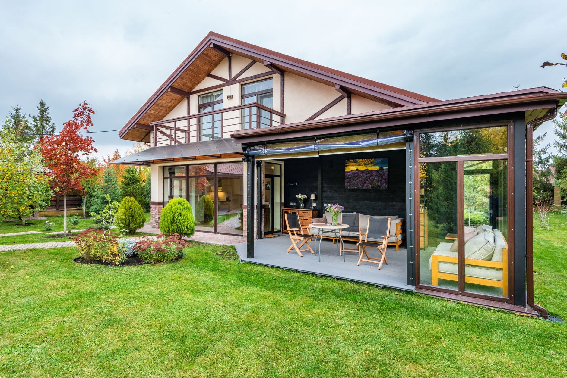 Villa met overdekte veranda en terras, omringd door een ruim gazon en bomen