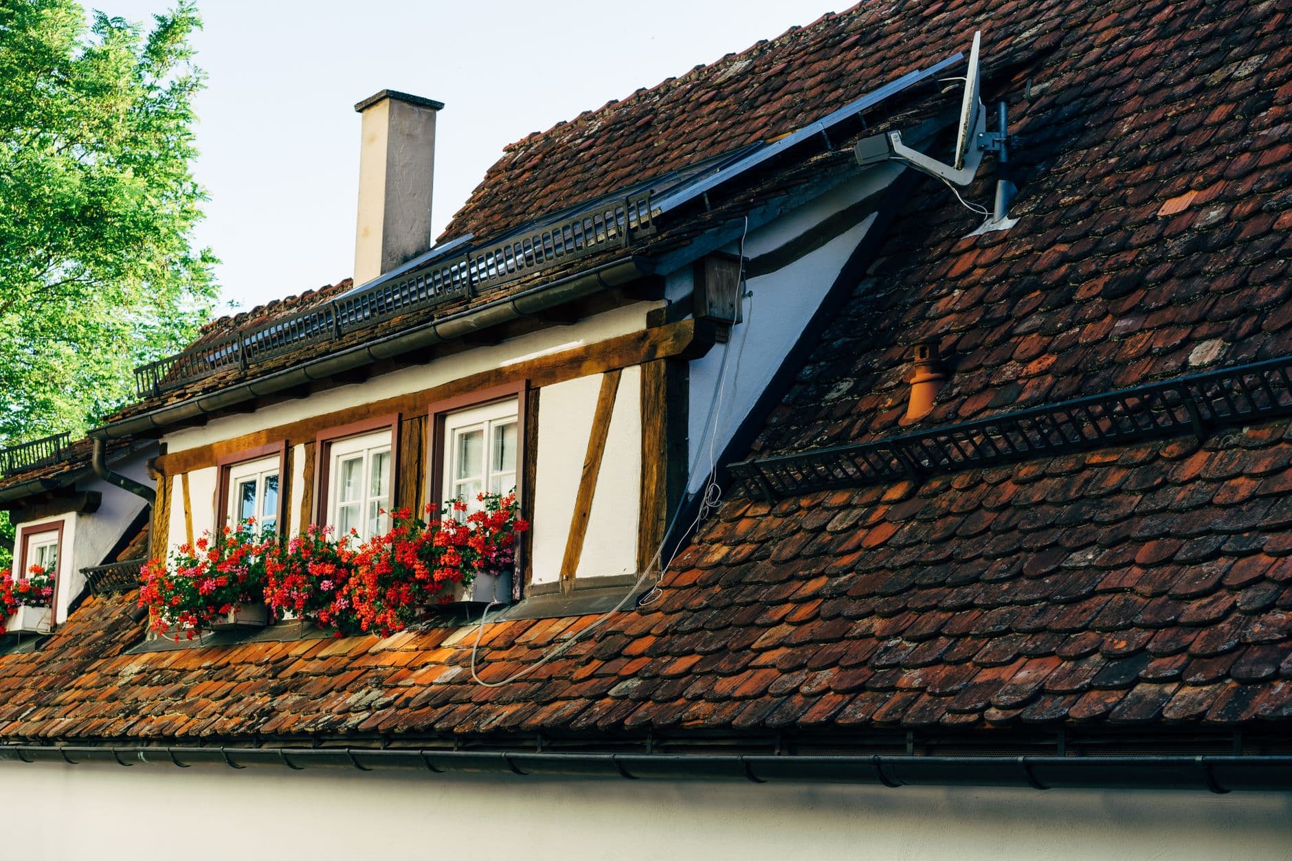 Rood pannendak met vakwerkgevel, bloembakken met geraniums en een schotelantenne
