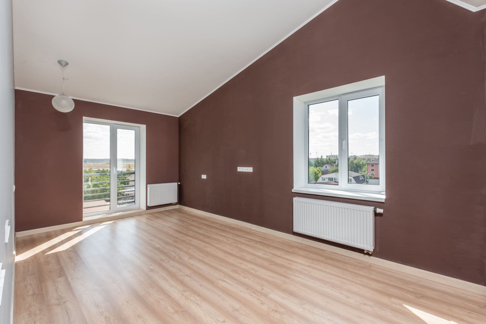 Lege gerenoveerde kamer met houten vloer, radiatoren, grote ramen en een hellend plafond