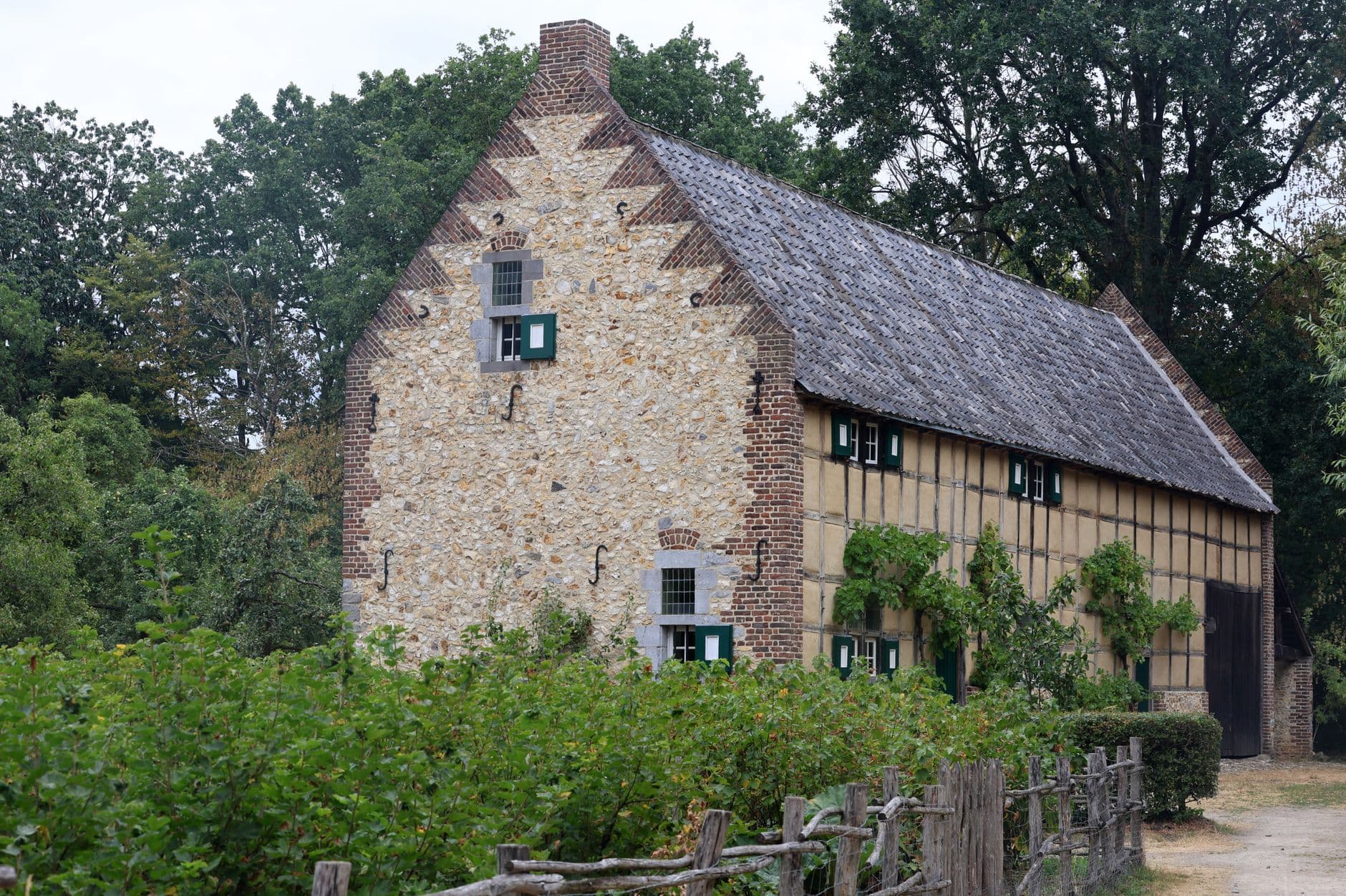 Historische hoeve met trapgevel in natuursteen en baksteen, omringd door groen