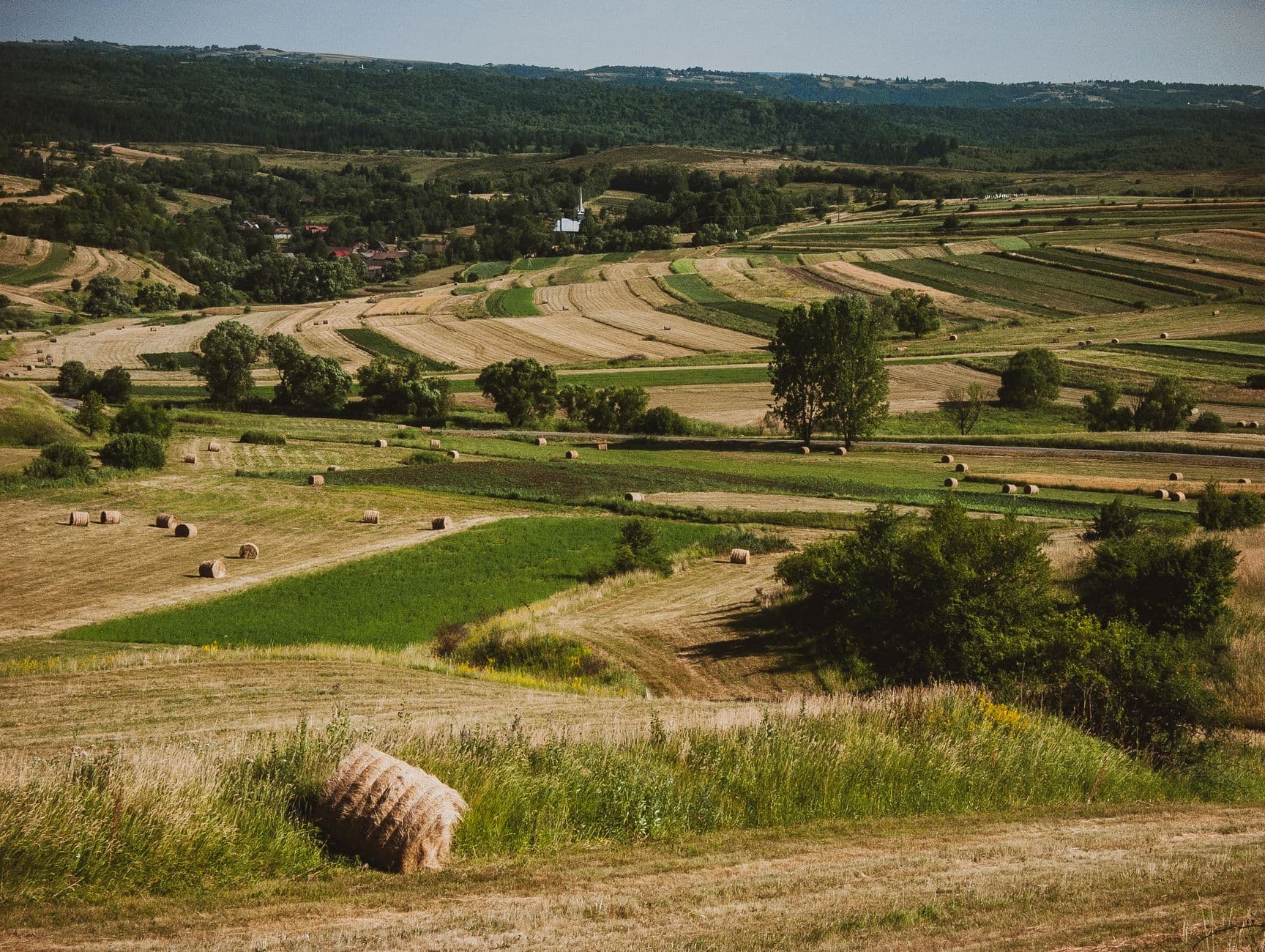 Glooiend landbouwlandschap met akkers, weiden en hooibalen onder een heldere lucht
