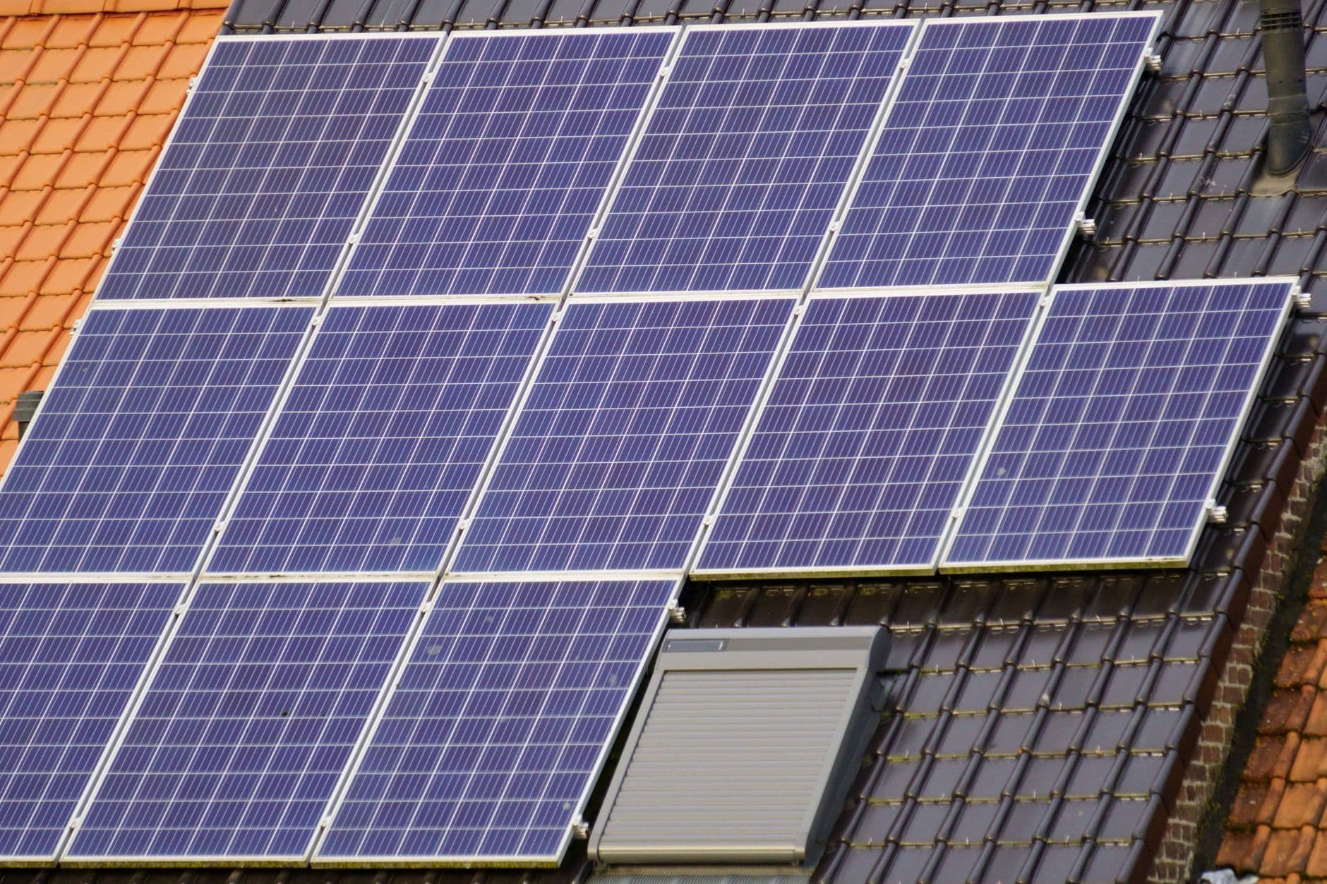 Zonnepanelen op een donker pannendak naast een oranje pannendak met bakstenen gevelrand