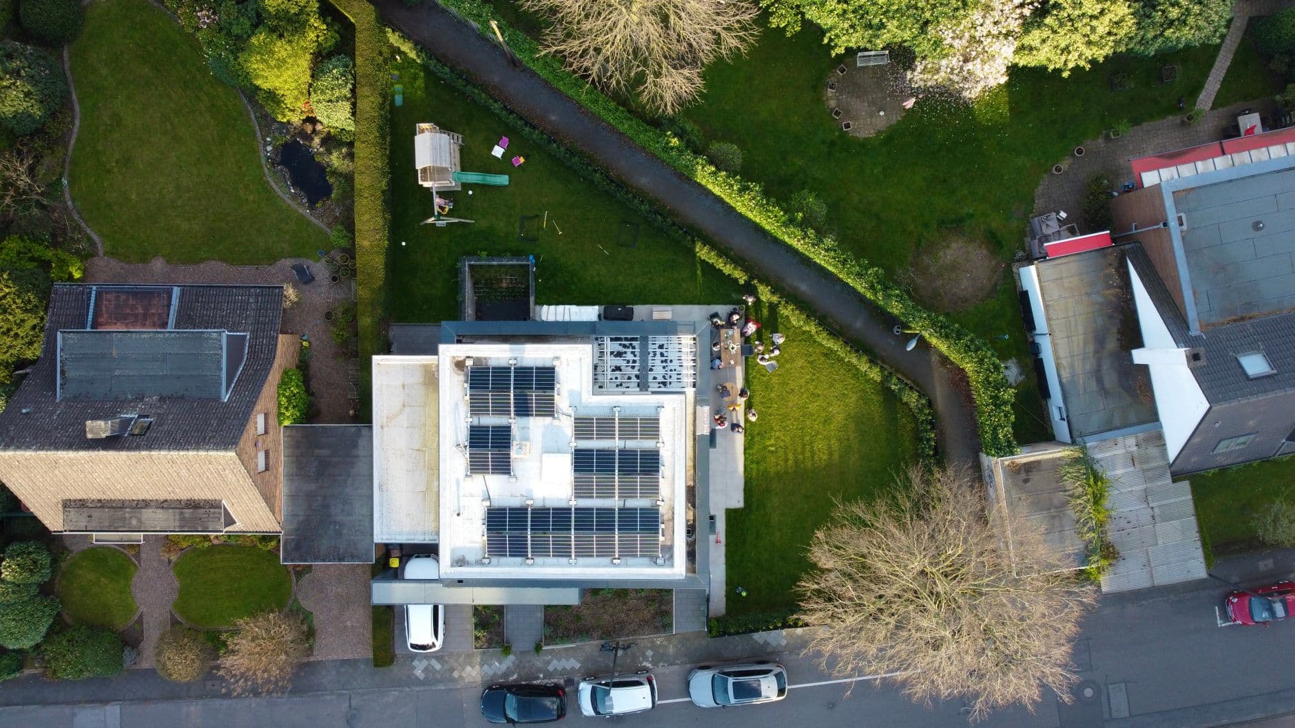Luchtbeeld van woningen met zonnepanelen op een plat dak, omringd door tuinen en bomen