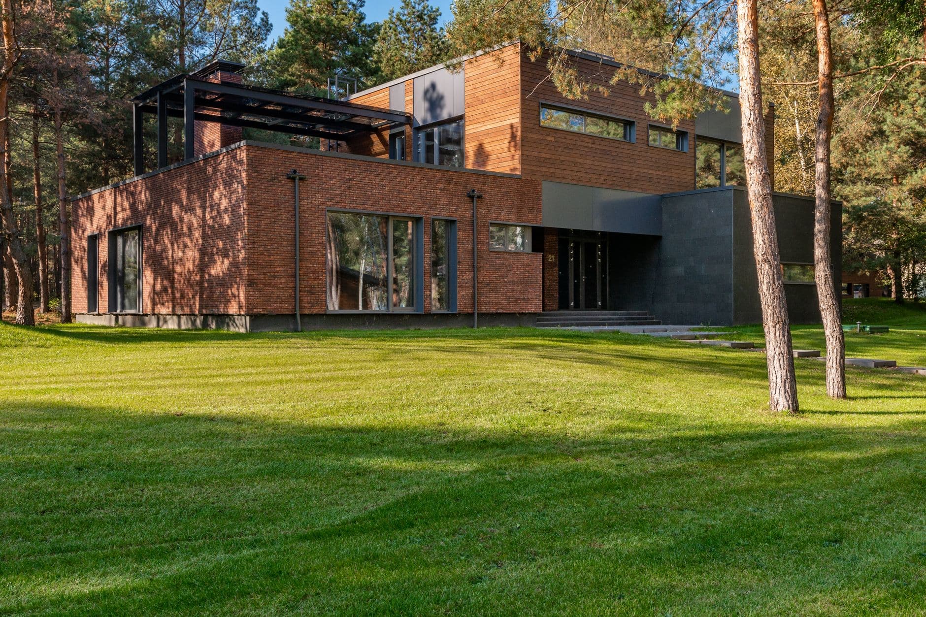 Moderne bakstenen woning met grote ramen op een groot grasveld tussen dennenbomen