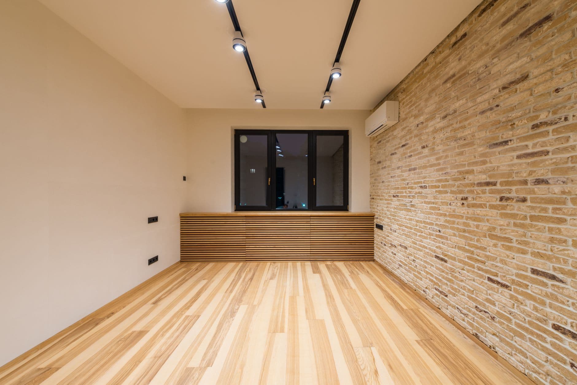 Lege kamer met houten vloer, bakstenen muur, spots op lichtrails en ingebouwde stopcontacten
