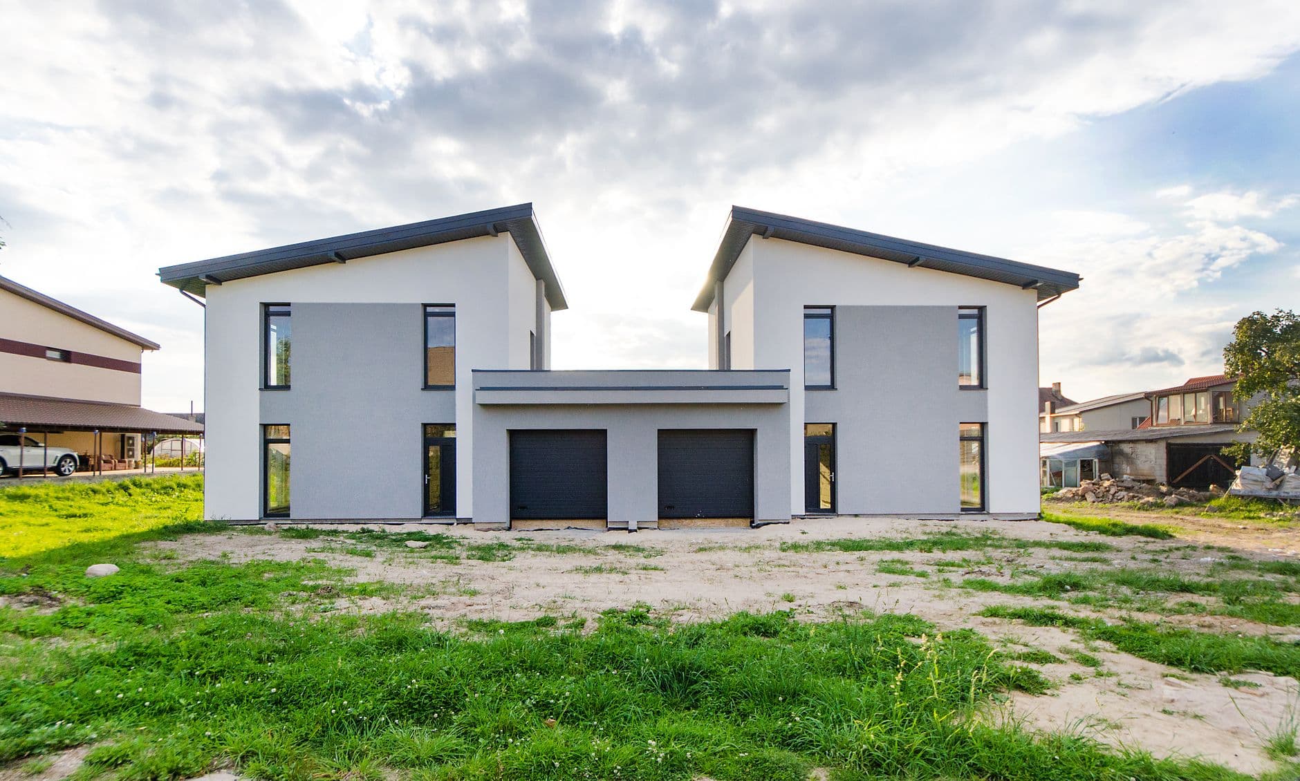 Twee nieuwgebouwde halfopen woningen met grijze gevels en garagepoorten onder een bewolkte lucht
