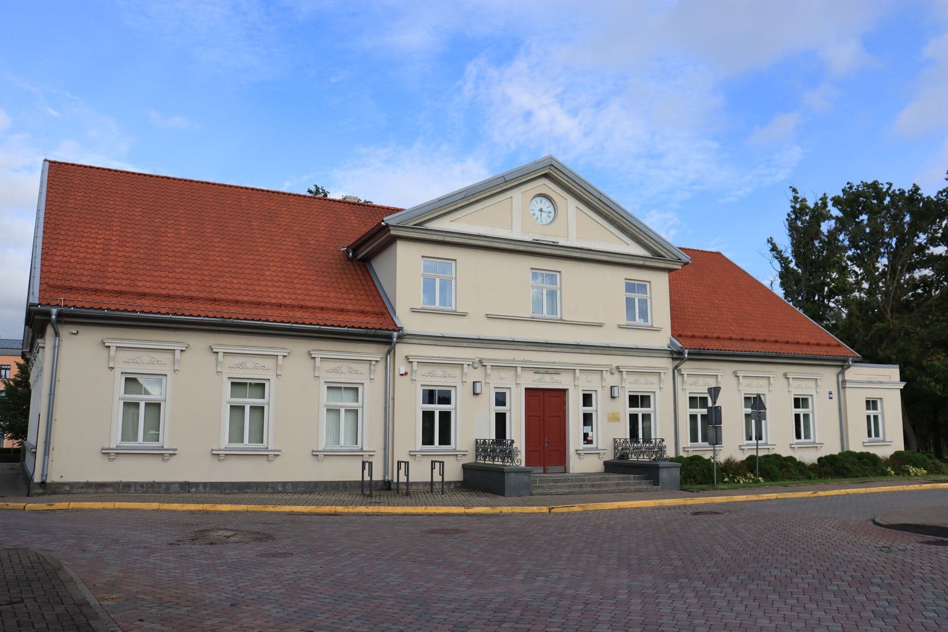 Historisch gepleisterd gebouw met rode pannendaken, klokgevel en een geplaveid plein onder blauwe lucht