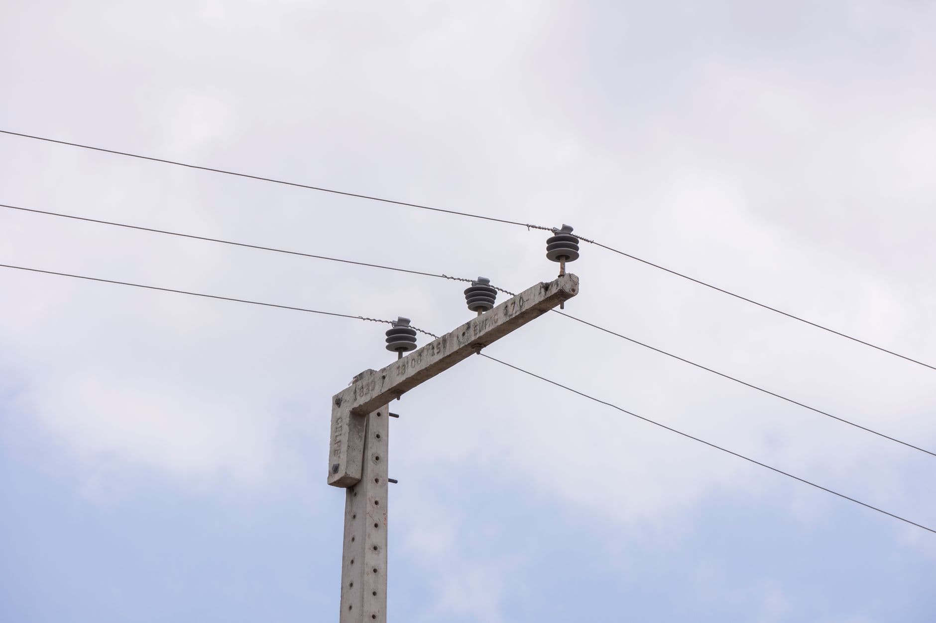 Betonnen elektriciteitspaal met isolatoren en bovengrondse leidingen tegen een bewolkte lucht