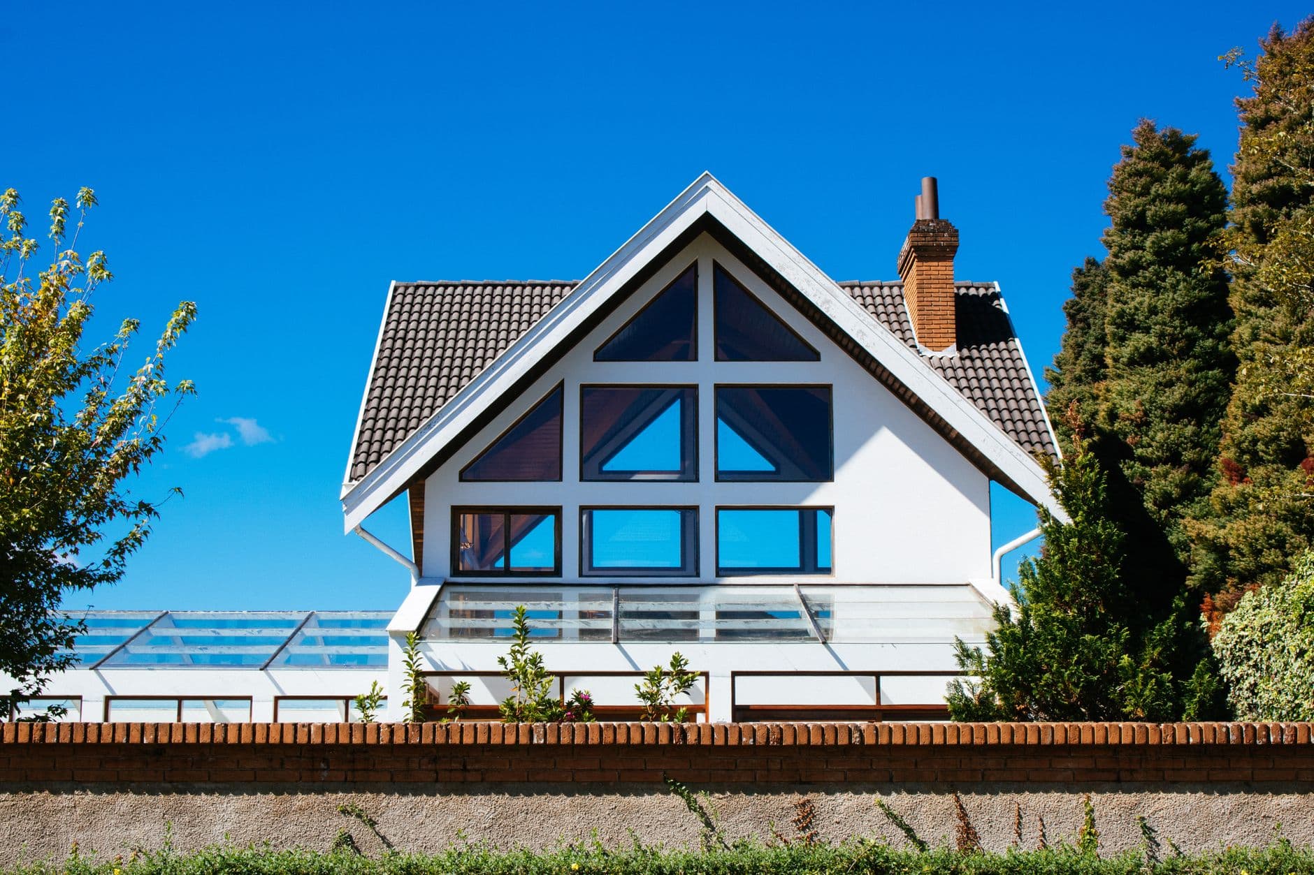 Witte villa met grote glazen puntgevel, pannendak en bakstenen schoorsteen achter een lage bakstenen muur