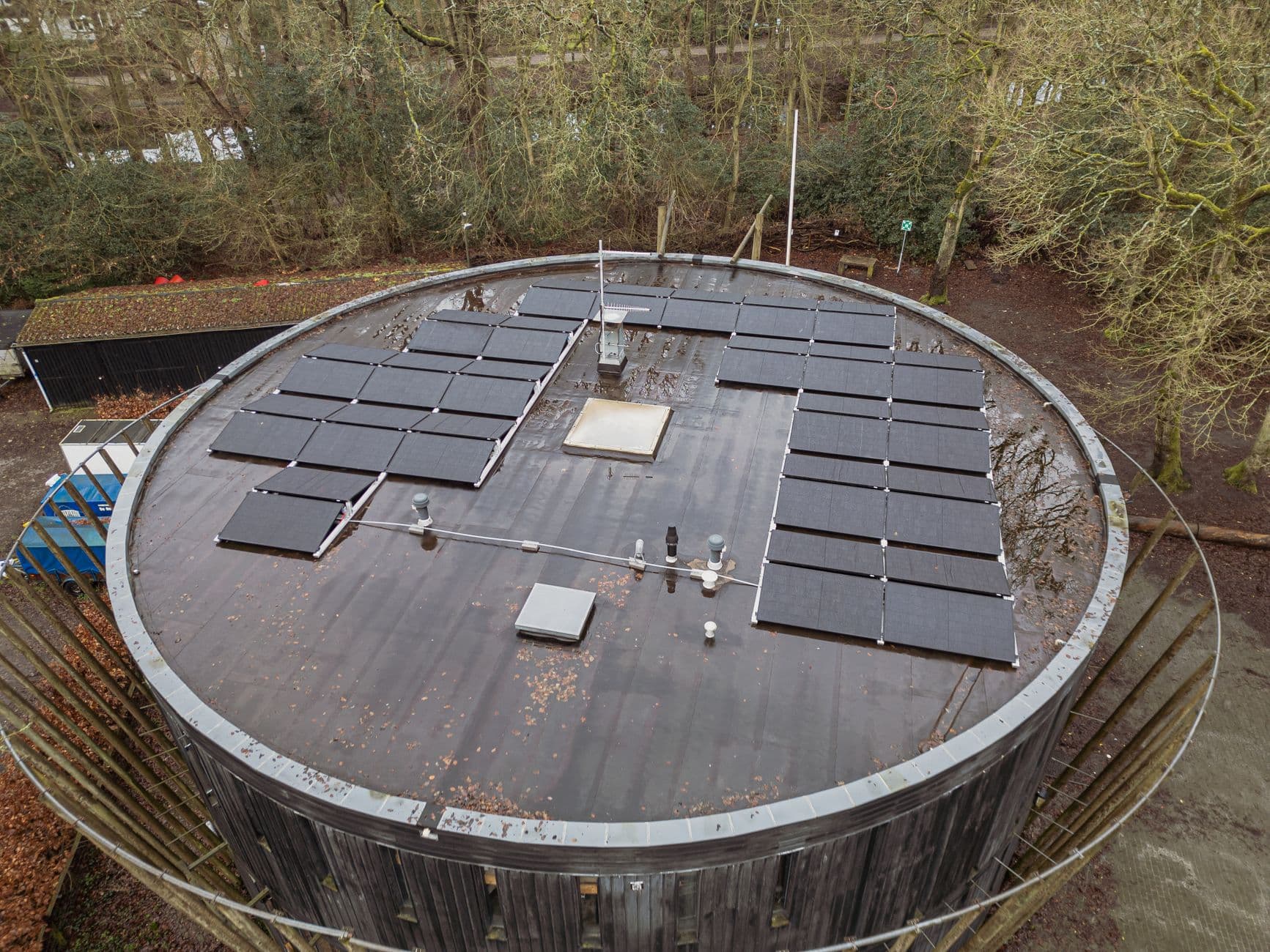 Luchtfoto van zonnepanelen op het platte ronde dak van een houten gebouw tussen de bomen