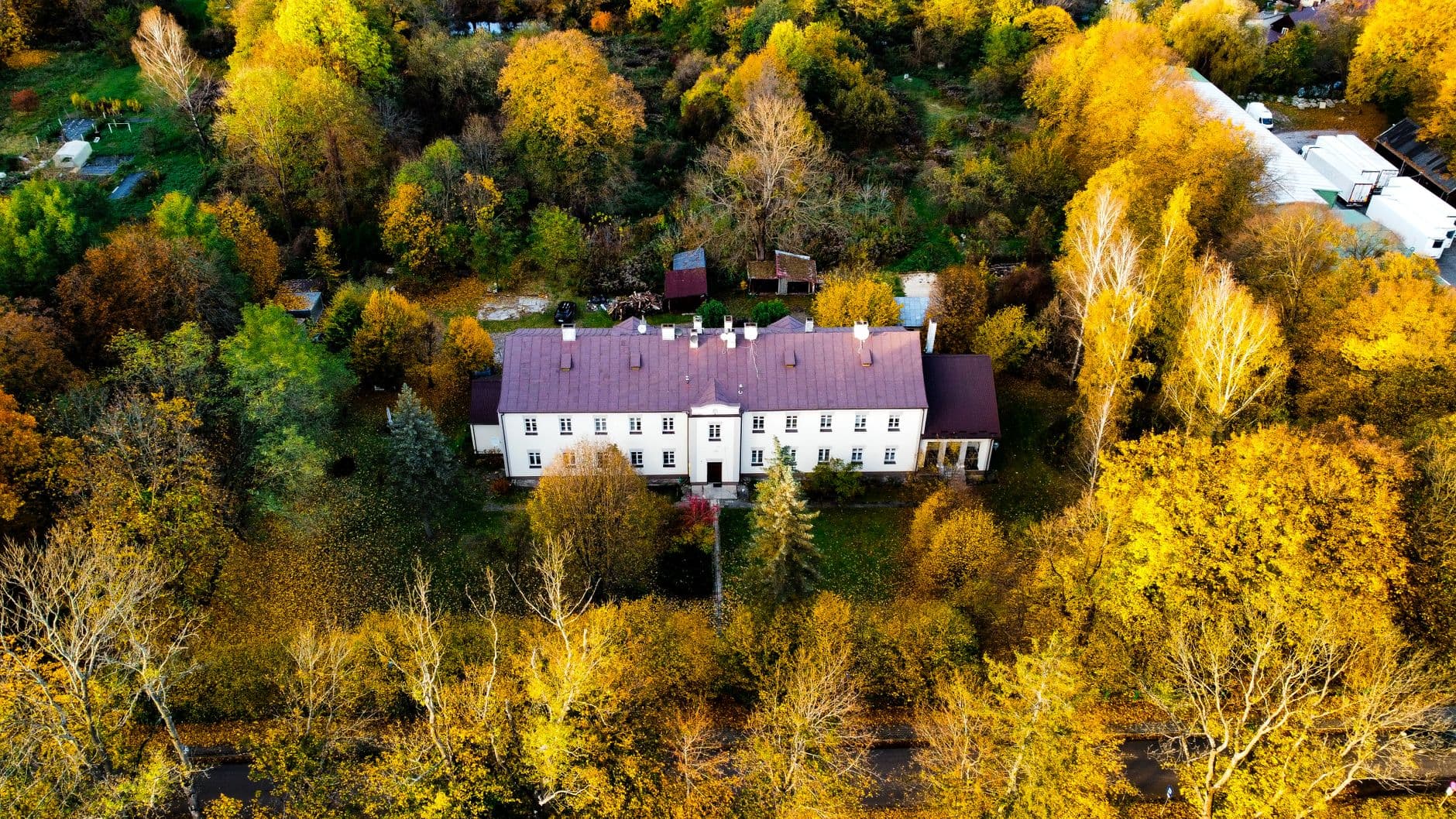 Luchtfoto van een wit landhuis met grijs dak, omringd door bomen in herfstkleuren