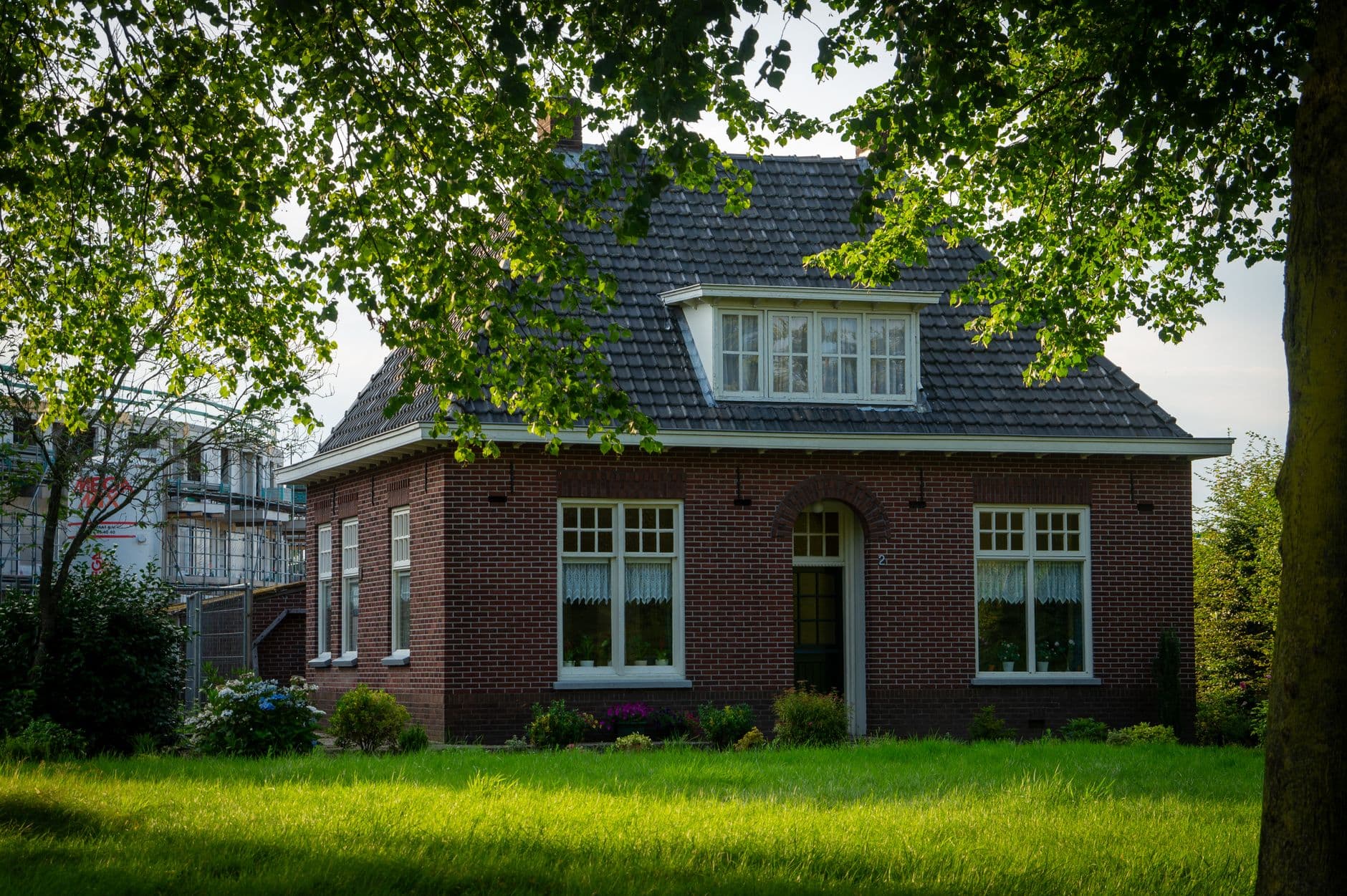 Vrijstaande rode bakstenen woning met dakkapel achter een grasperk en bomen