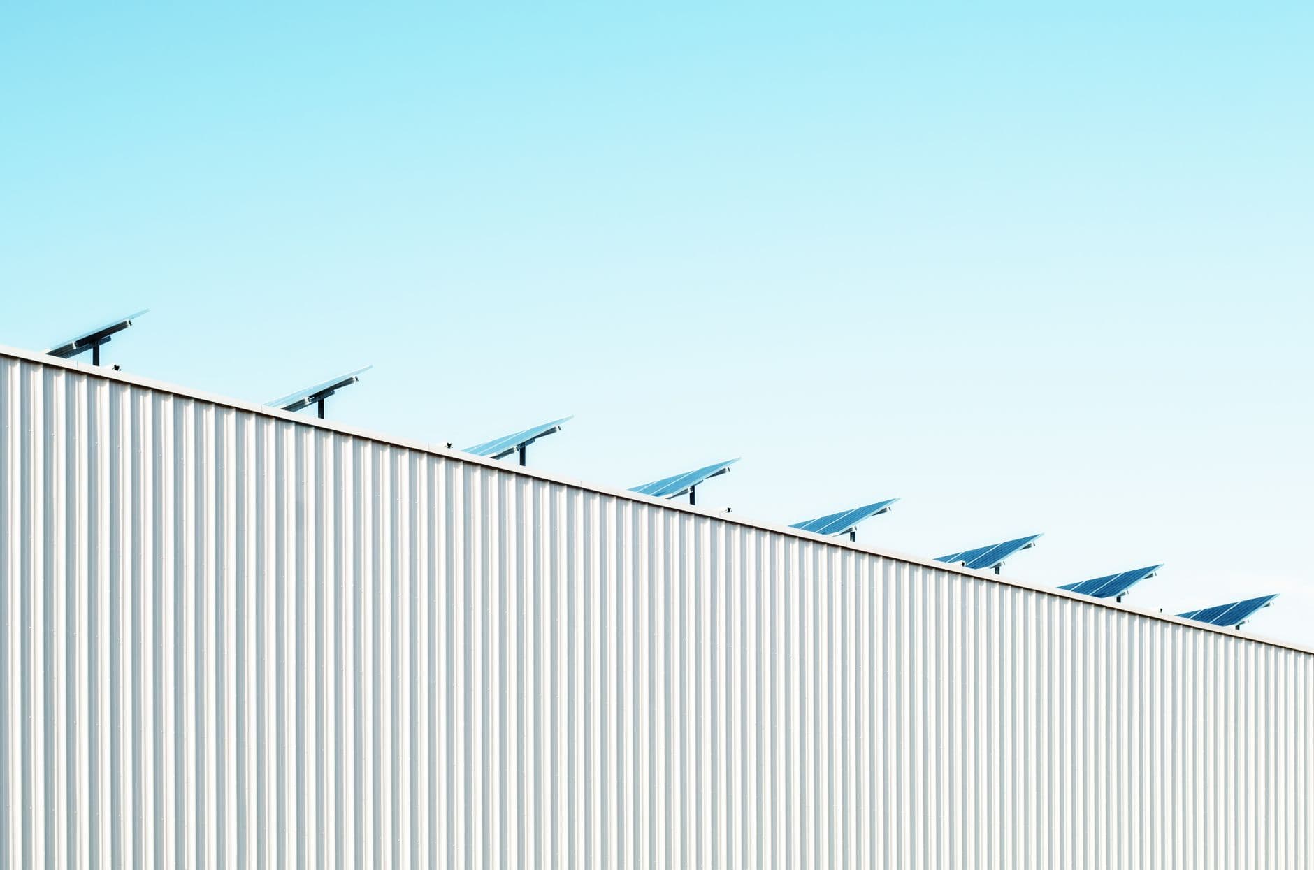 Rij zonnepanelen op de dakrand van een gebouw met een gegolfde metalen gevel onder een blauwe lucht