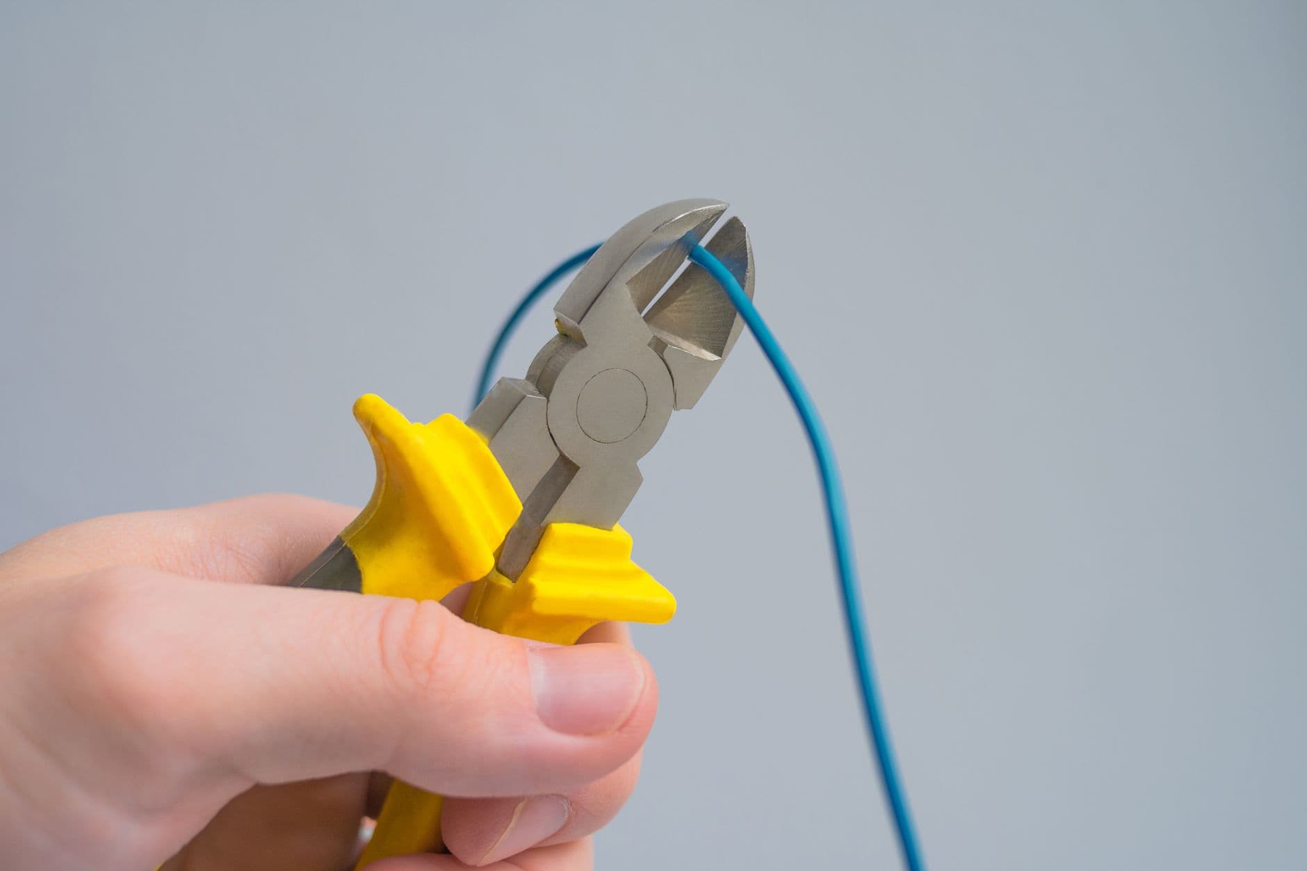 Hand knipt met een kniptang een blauwe elektriciteitsdraad door