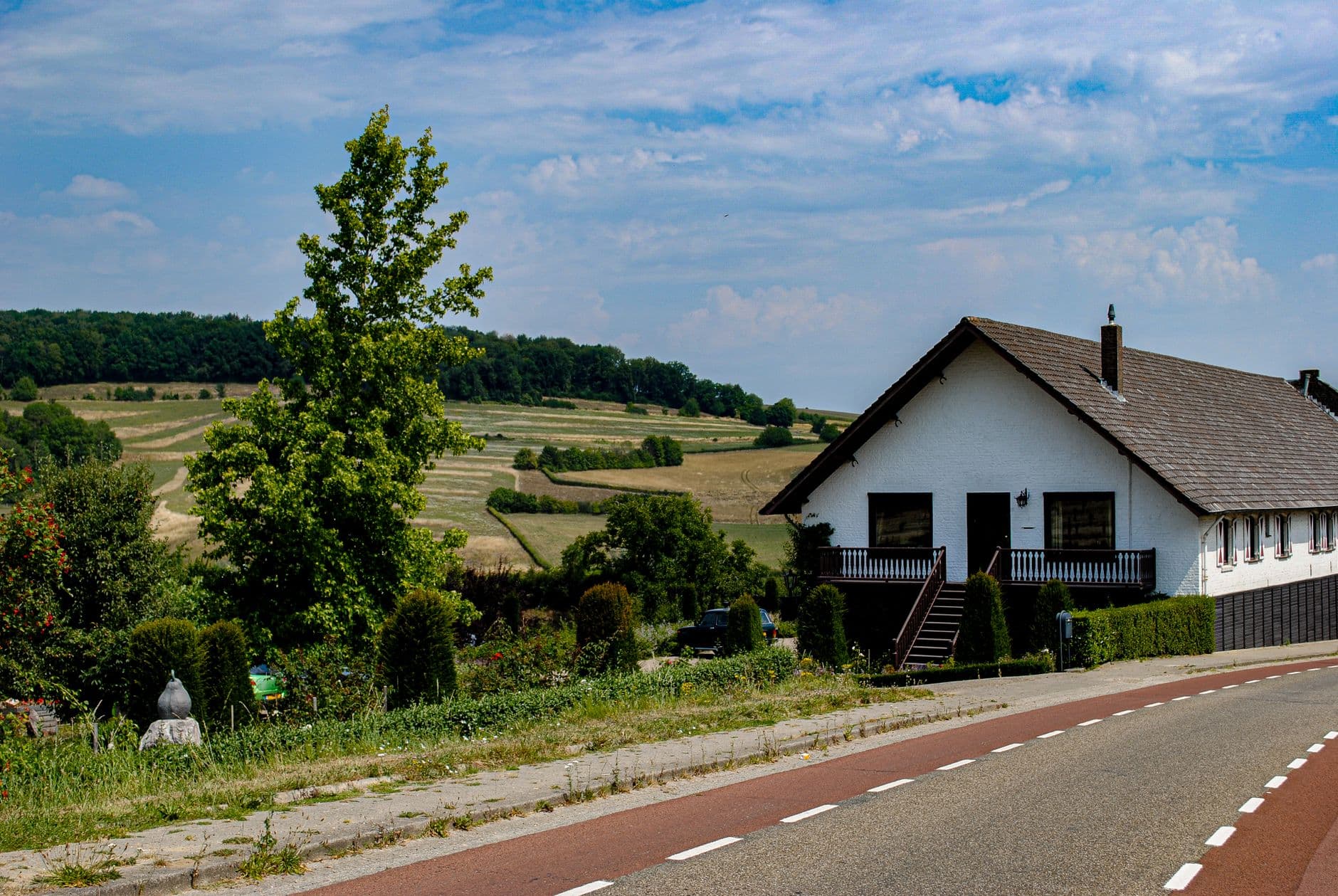 Witte woning met donker pannendak langs een landweg met rode fietsstroken en glooiende velden