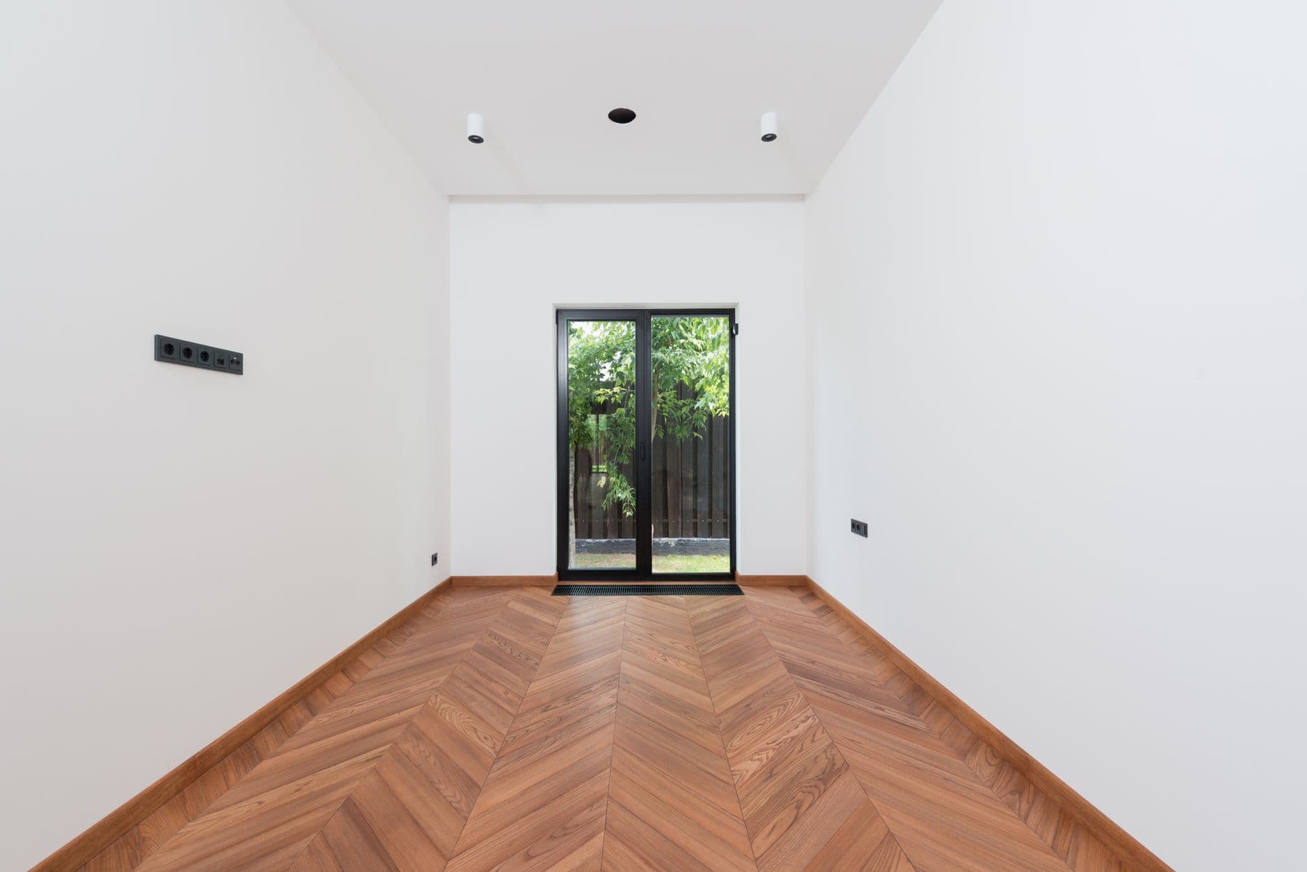 Lege, pas gerenoveerde kamer met witte muren, visgraatparket, inbouwspots en stopcontacten