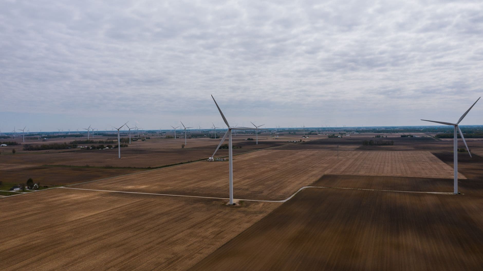 Windturbines tussen omgeploegde akkers onder een grijze wolkenlucht
