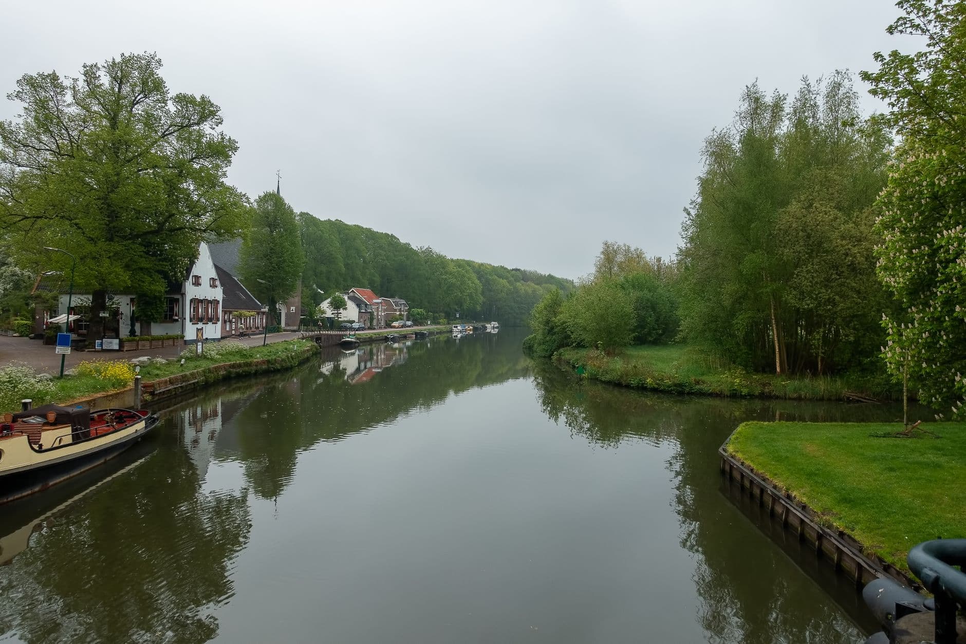 Rustig kanaal met bomen langs de oevers, woningen en aangemeerde boten op een bewolkte dag