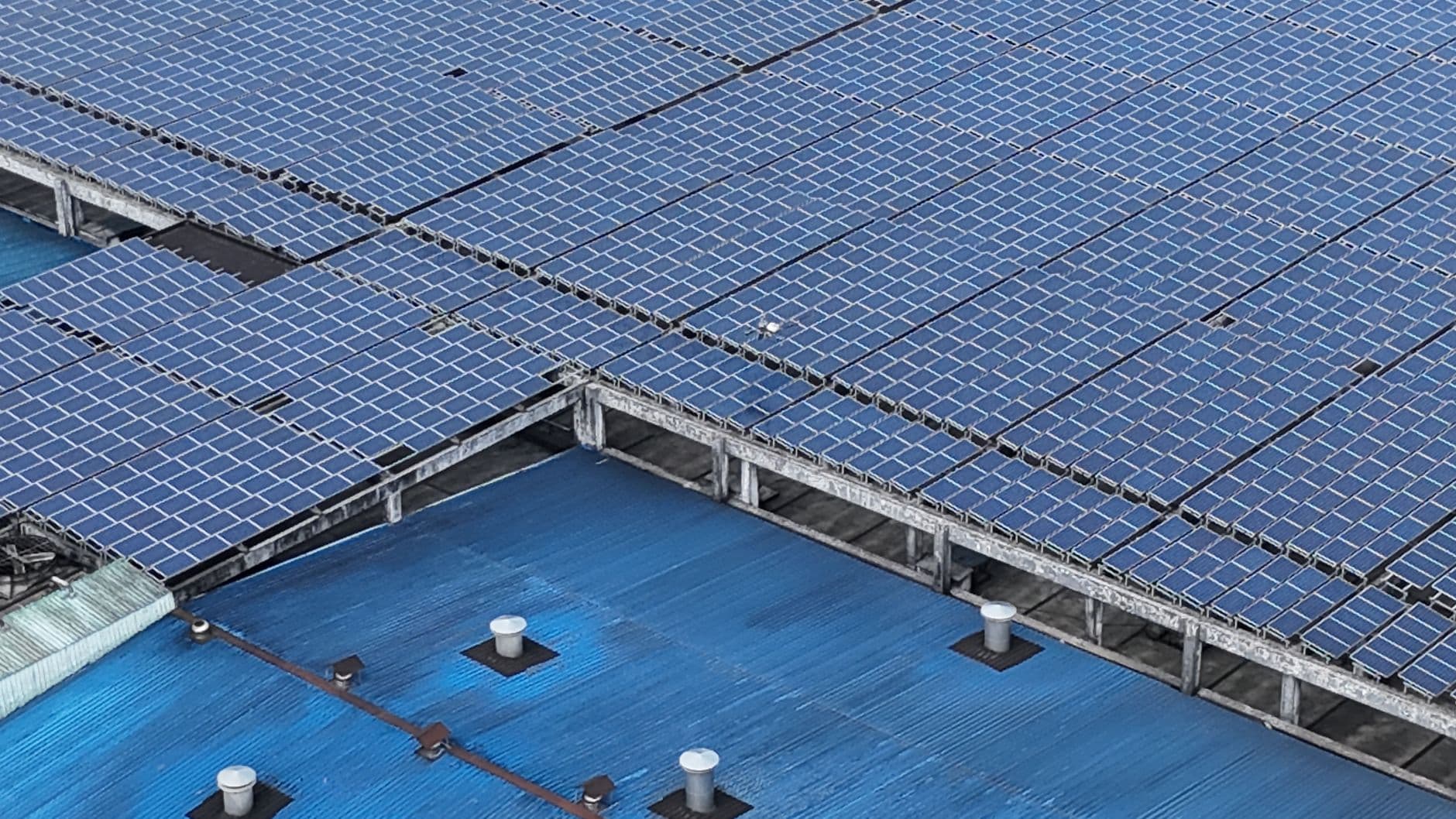 Rijen zonnepanelen op een blauw industrieel dak, van bovenaf gezien