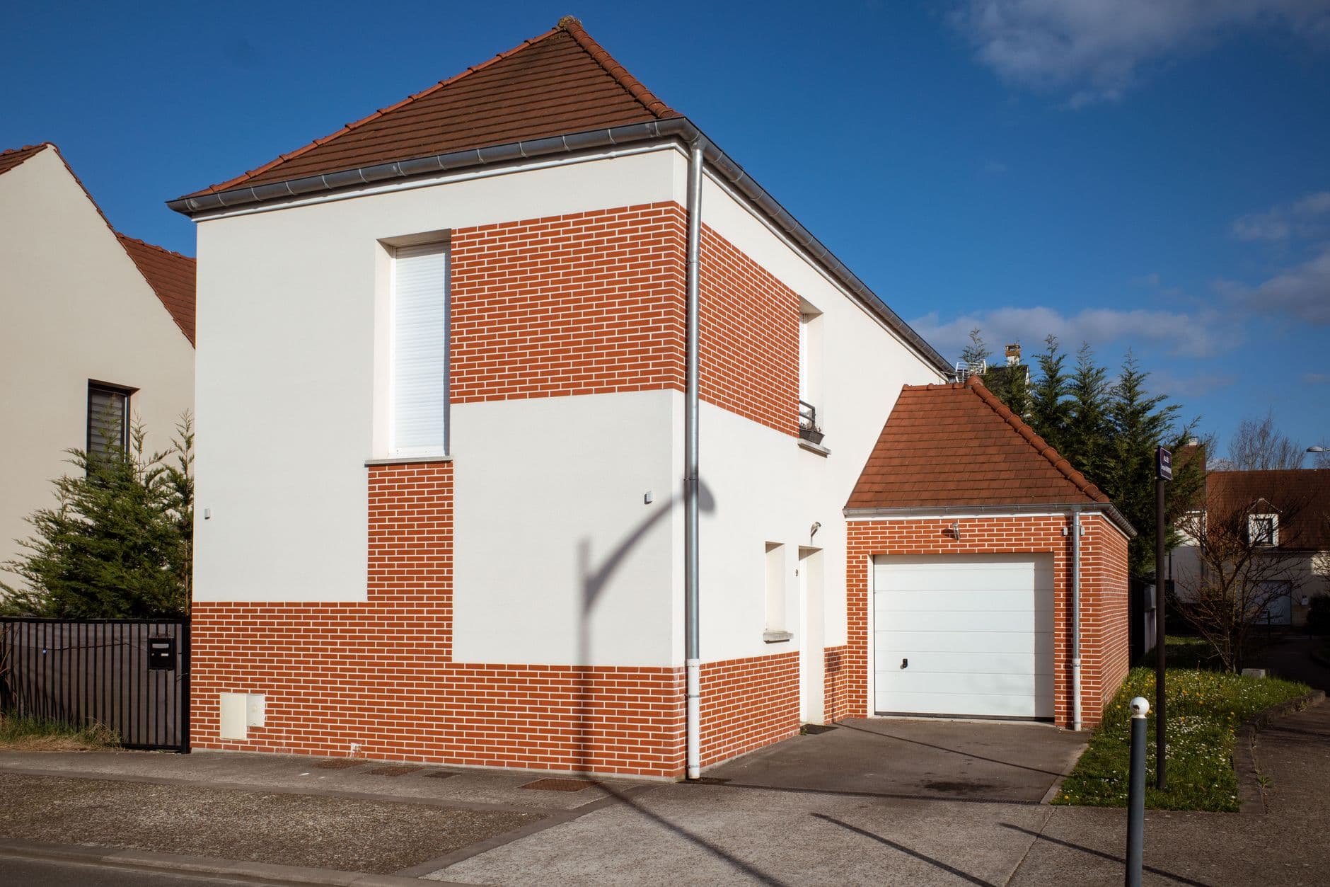 Moderne woning met rode baksteen en witte gevel, pannendak en garage onder een blauwe lucht