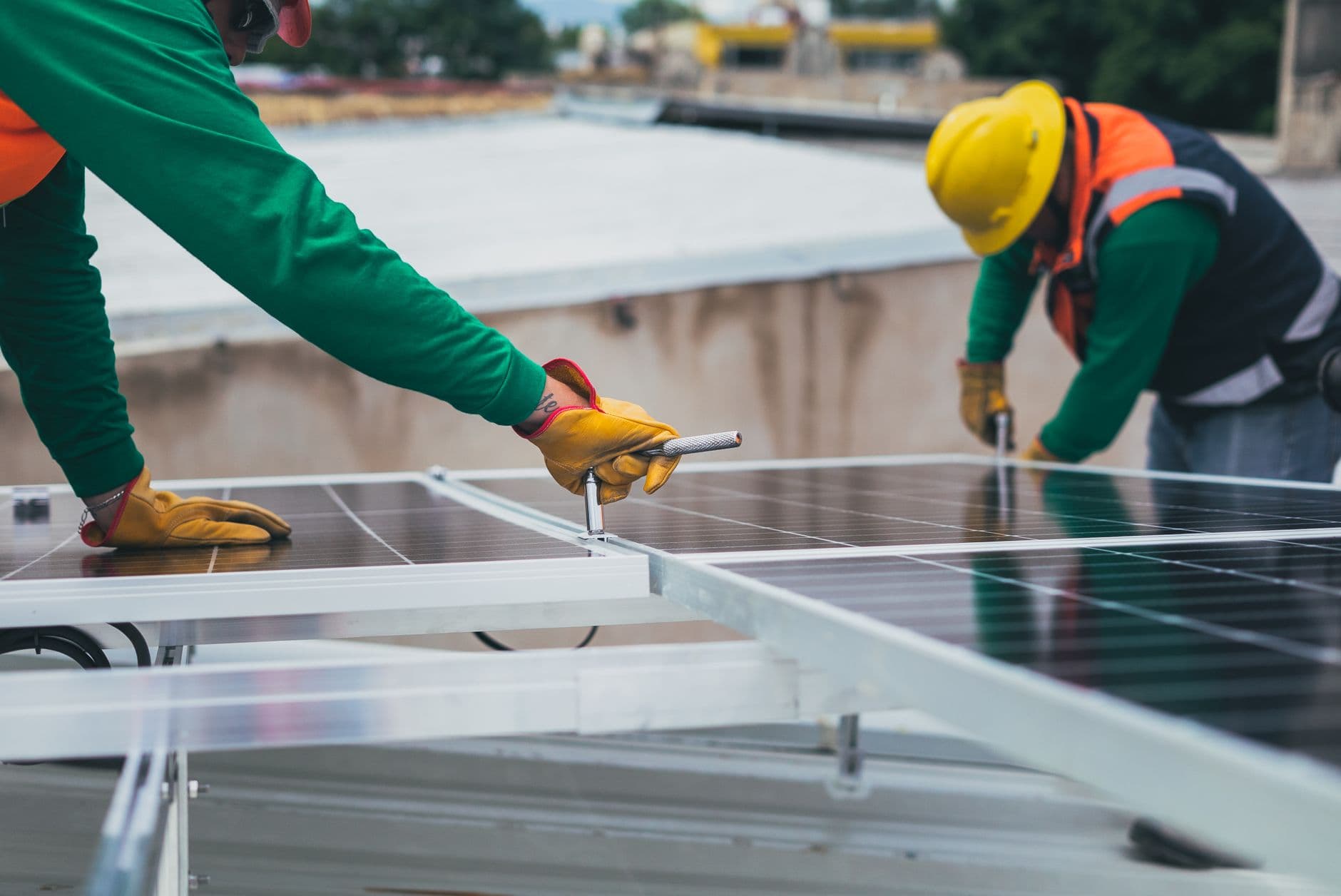 Twee installateurs met werkhandschoenen bevestigen zonnepanelen op een plat dak