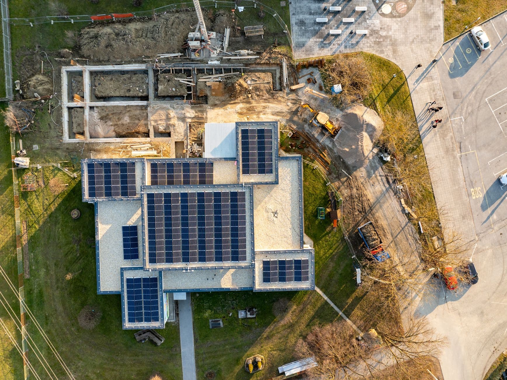 Luchtbeeld van een plat dak vol zonnepanelen naast een bouwwerf met graafmachines