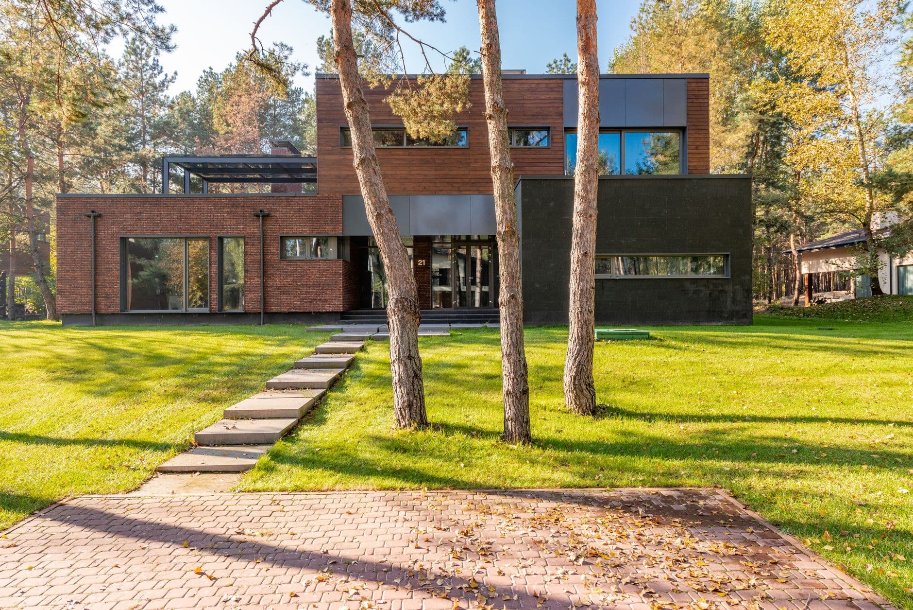 Moderne bakstenen woning met grote ramen, een gazon en dennenbomen in de herfstzon
