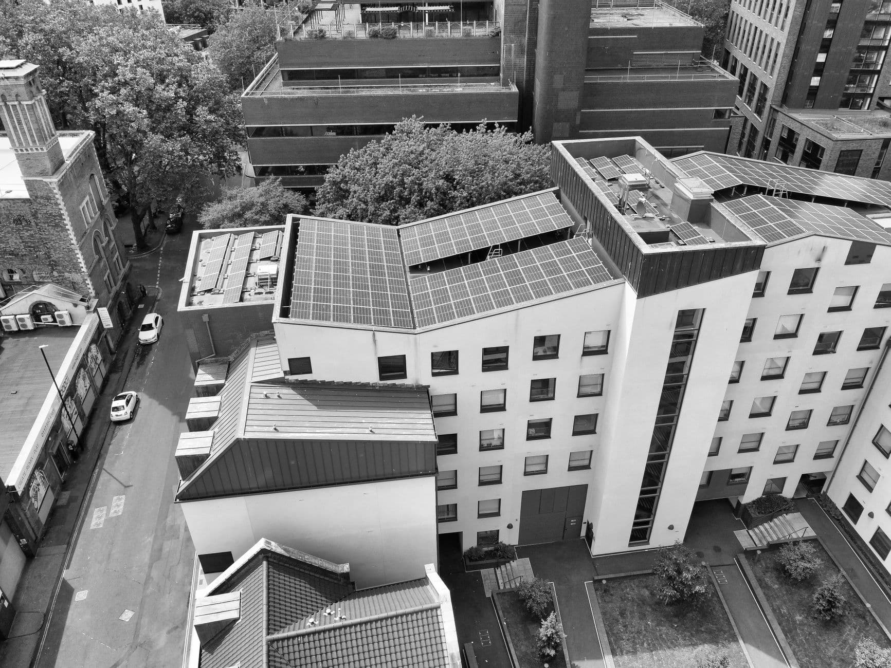 Zwart-wit luchtbeeld van platte daken met zonnepanelen tussen woningen en appartementen