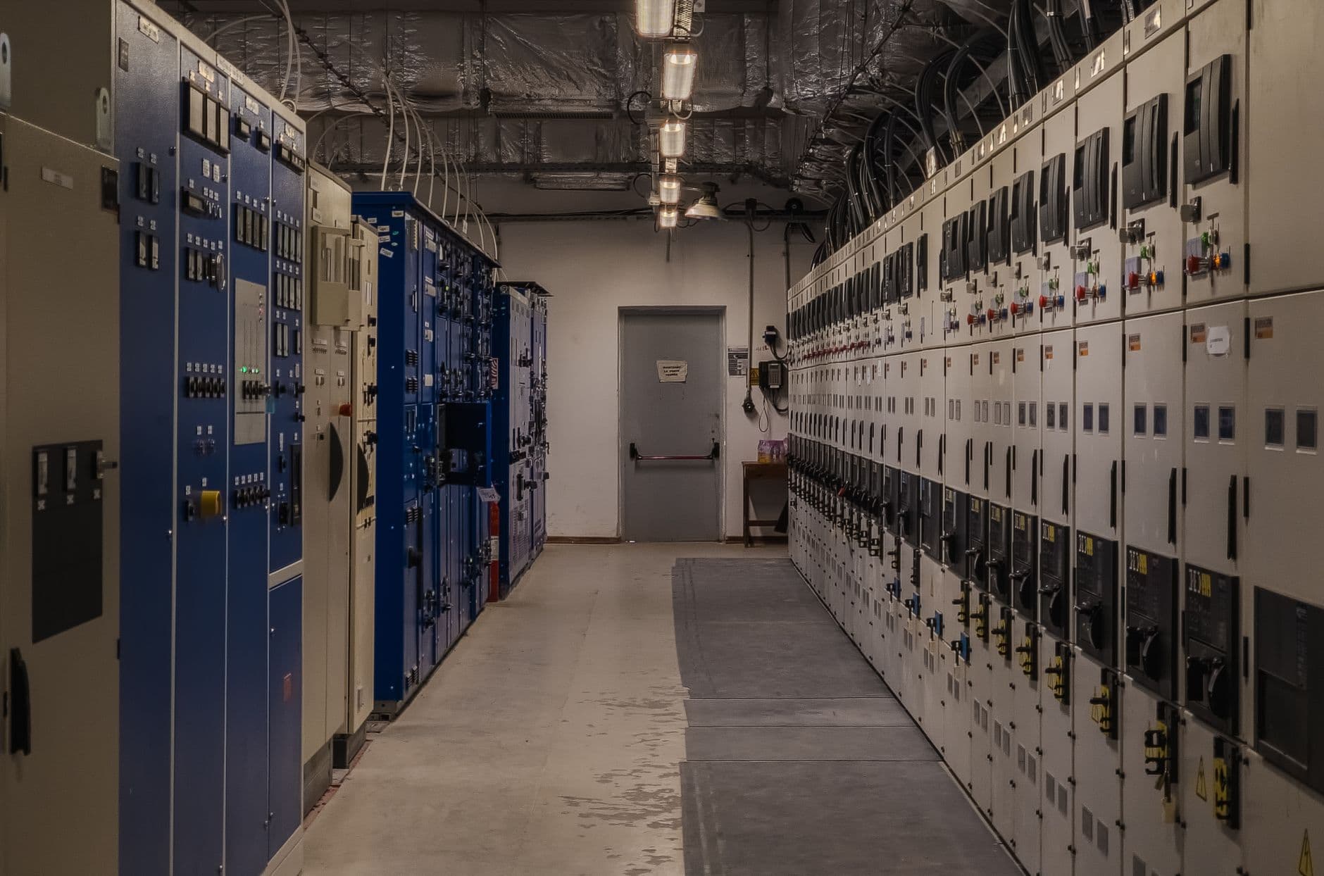 Lange technische ruimte met rijen elektrische schakelkasten en bekabeling aan het plafond