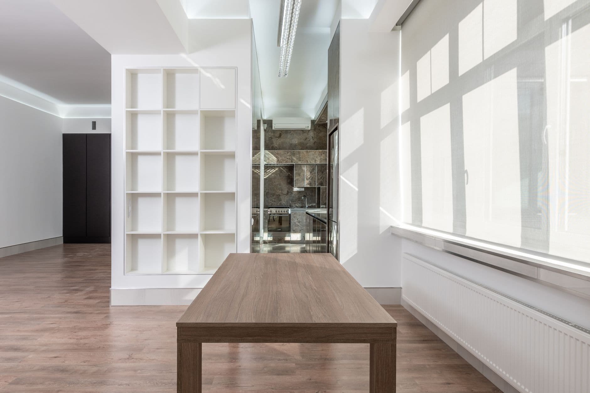 Lichte lege ruimte met houten tafel, open wandkast, radiator en ledverlichting aan het plafond