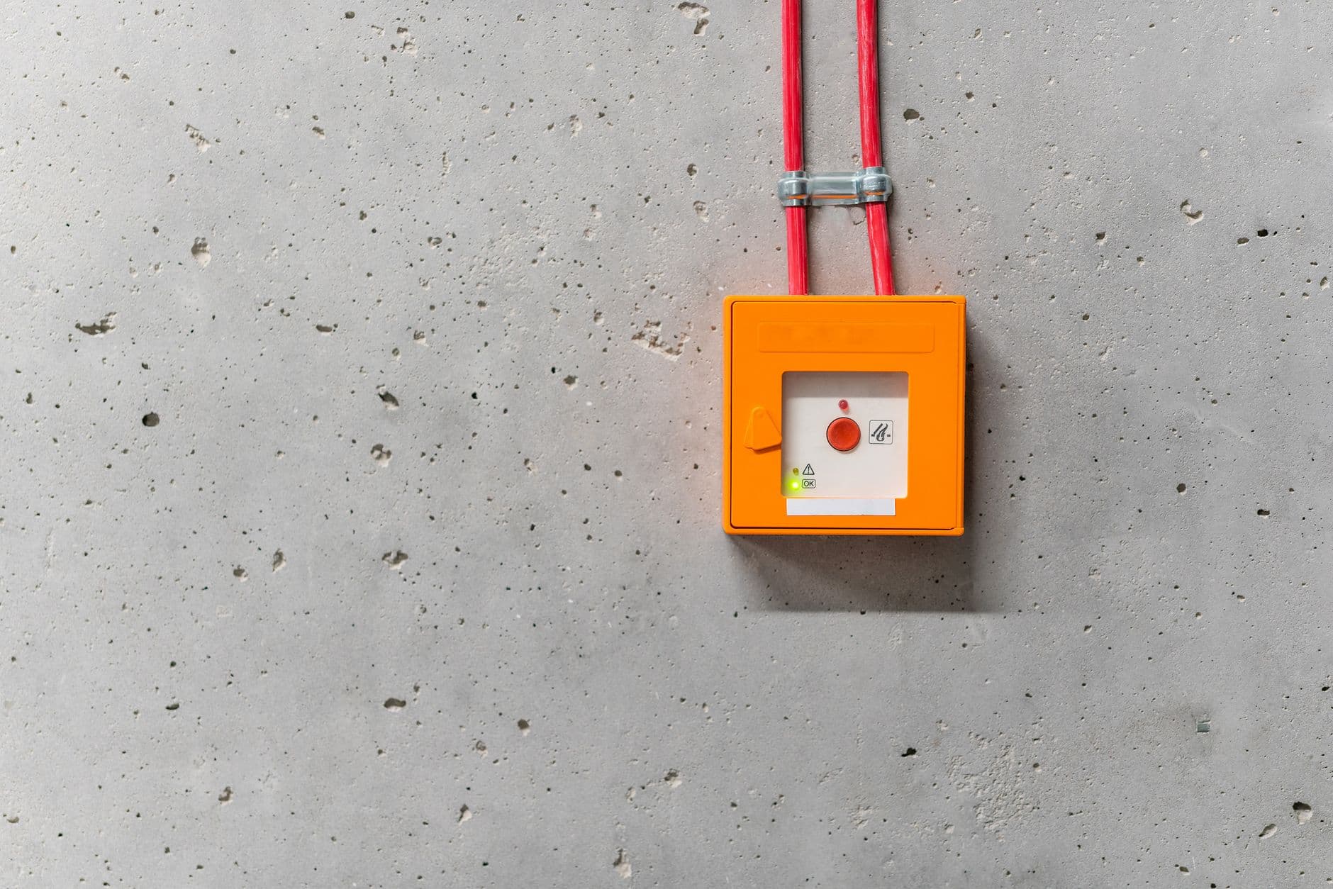 Oranje noodknop met rode kabels gemonteerd op een ruwe betonnen muur